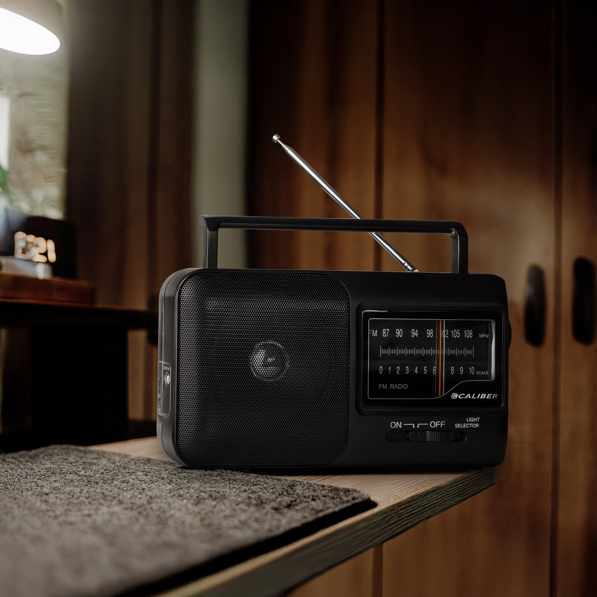 Black retro radio with a handle, antenna, and tuning dial, set on a wooden surface.