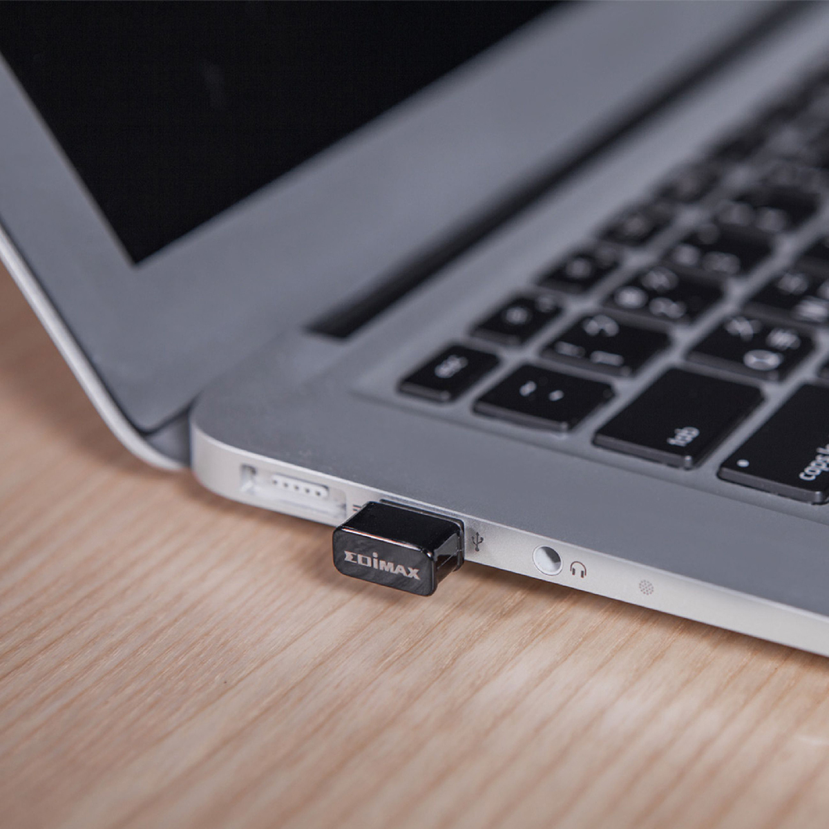 A black Edimax USB adapter plugged into a silver laptop on a wooden table.