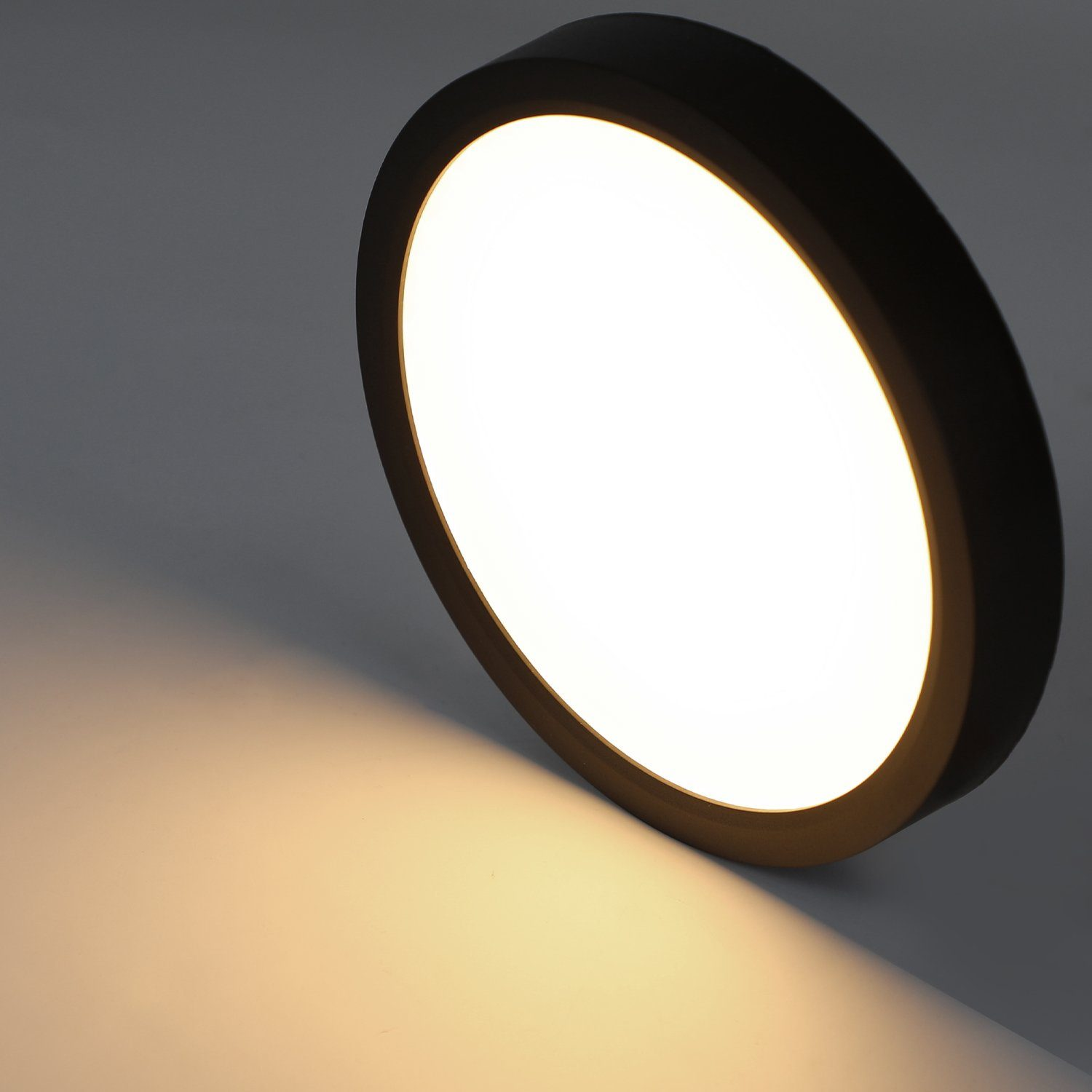 Una luce LED rotonda con bordo nero che emette una luce bianca brillante, proiettando un bagliore su una superficie grigio chiaro.
