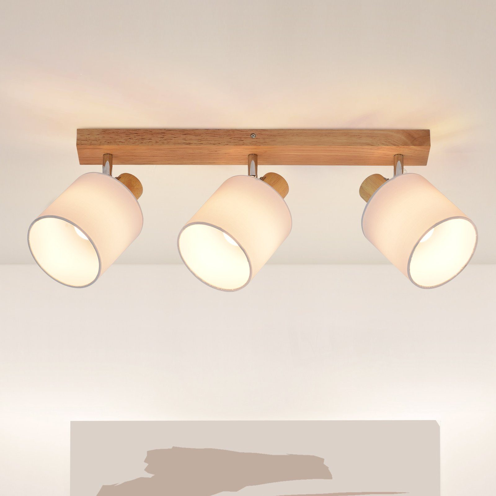 Una plafoniera con tre paralumi bianchi su una trave di legno. Le luci sono orientate verso il basso.