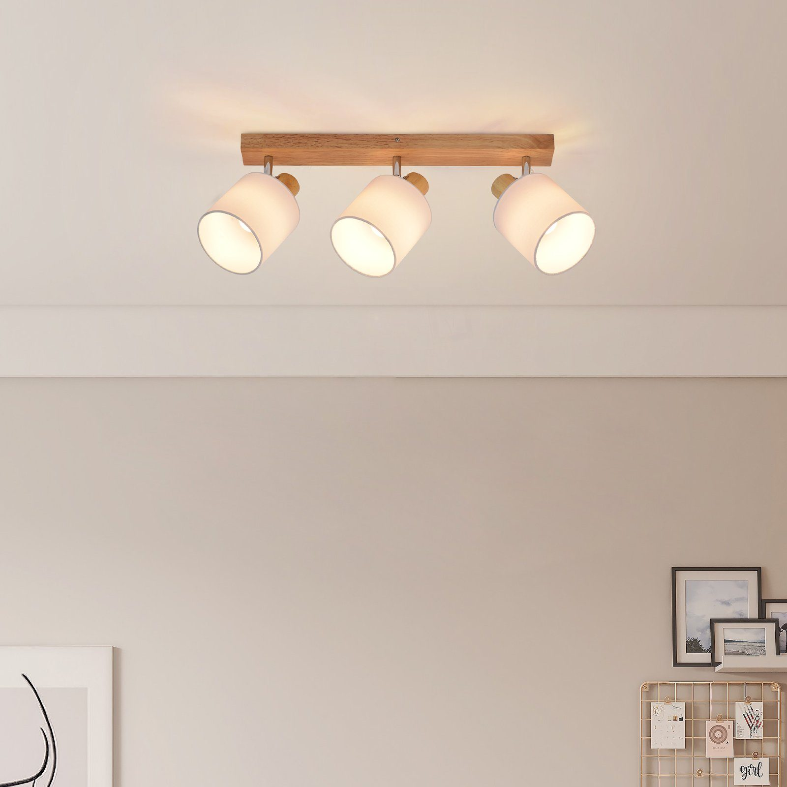 Tre faretti bianchi su una trave di legno attaccata a un soffitto bianco. Sfondo bianco.