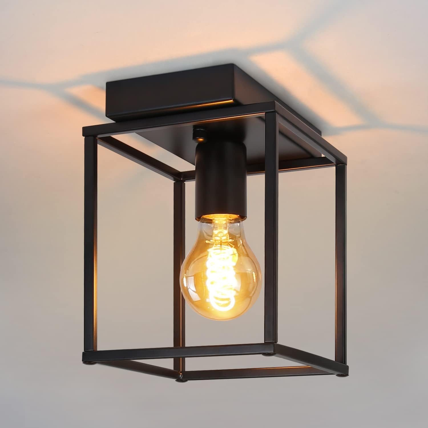 Lampada da soffitto in metallo nero con lampadina visibile. La lampadina brilla calda.