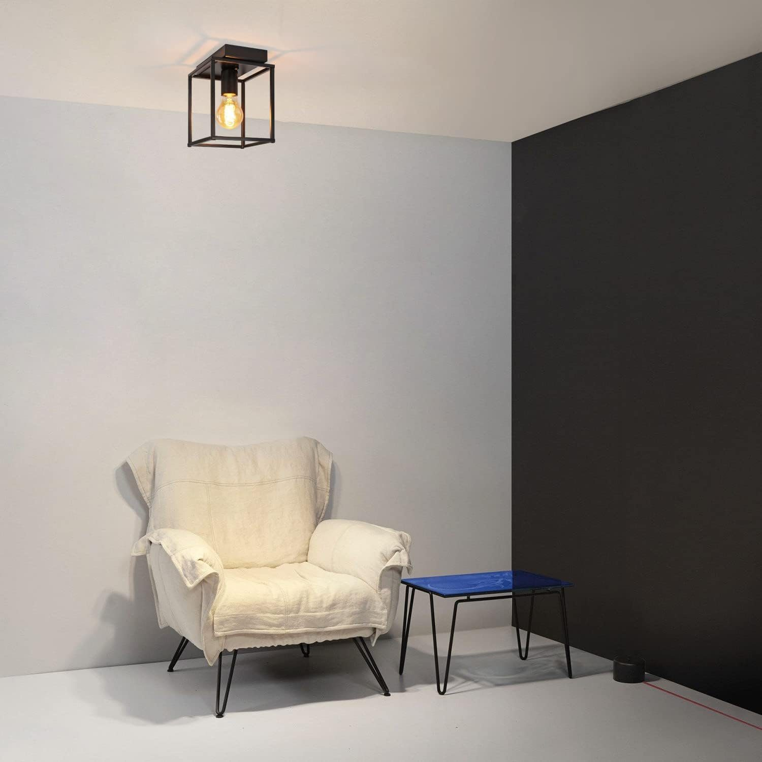 Moderner Raum mit weißen und schwarzen Wänden, weißem Sessel, blauem Tisch und quadratischer Leuchte.