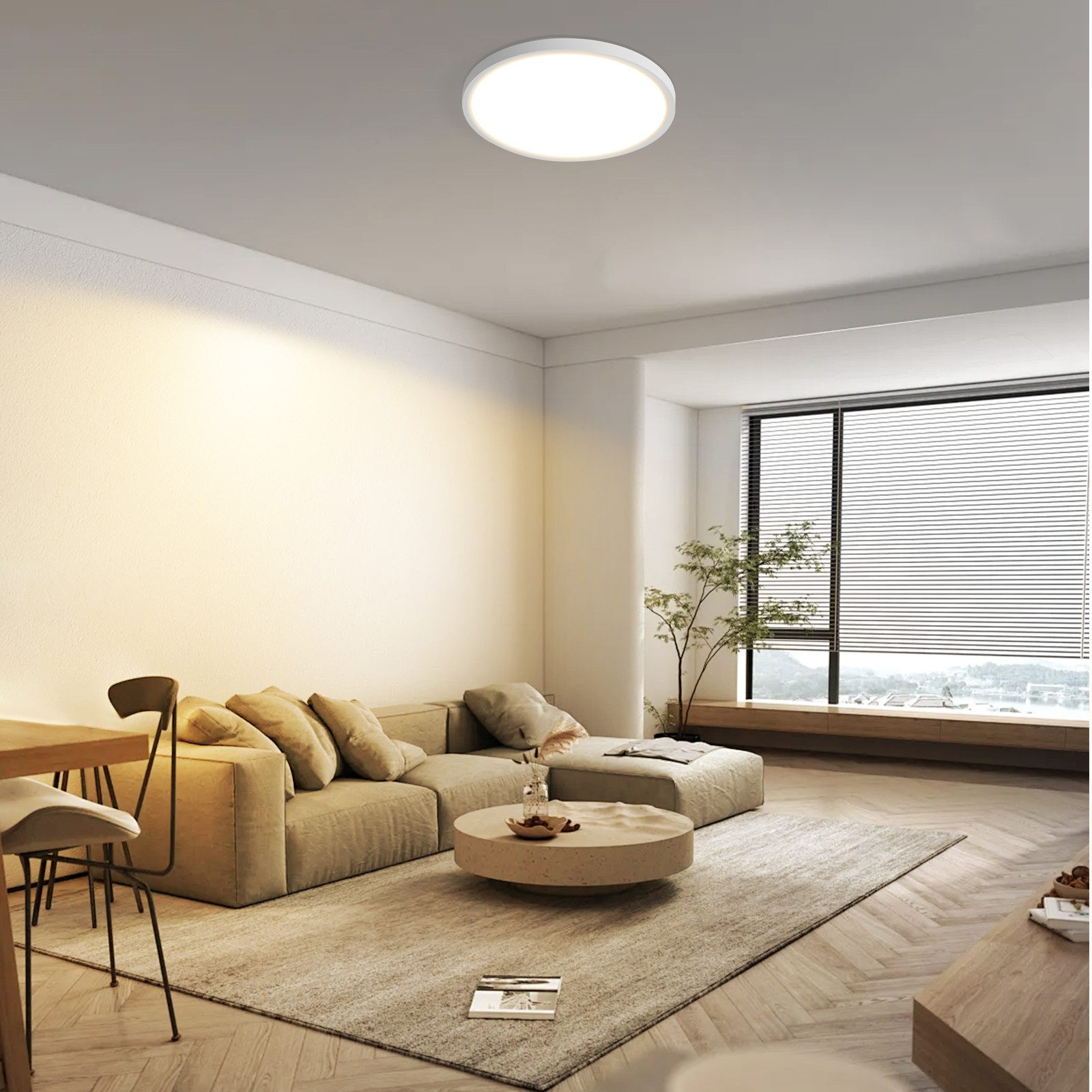 Ein modernes Wohnzimmer mit beigem Sofa, rundem Couchtisch und großem Fenster.