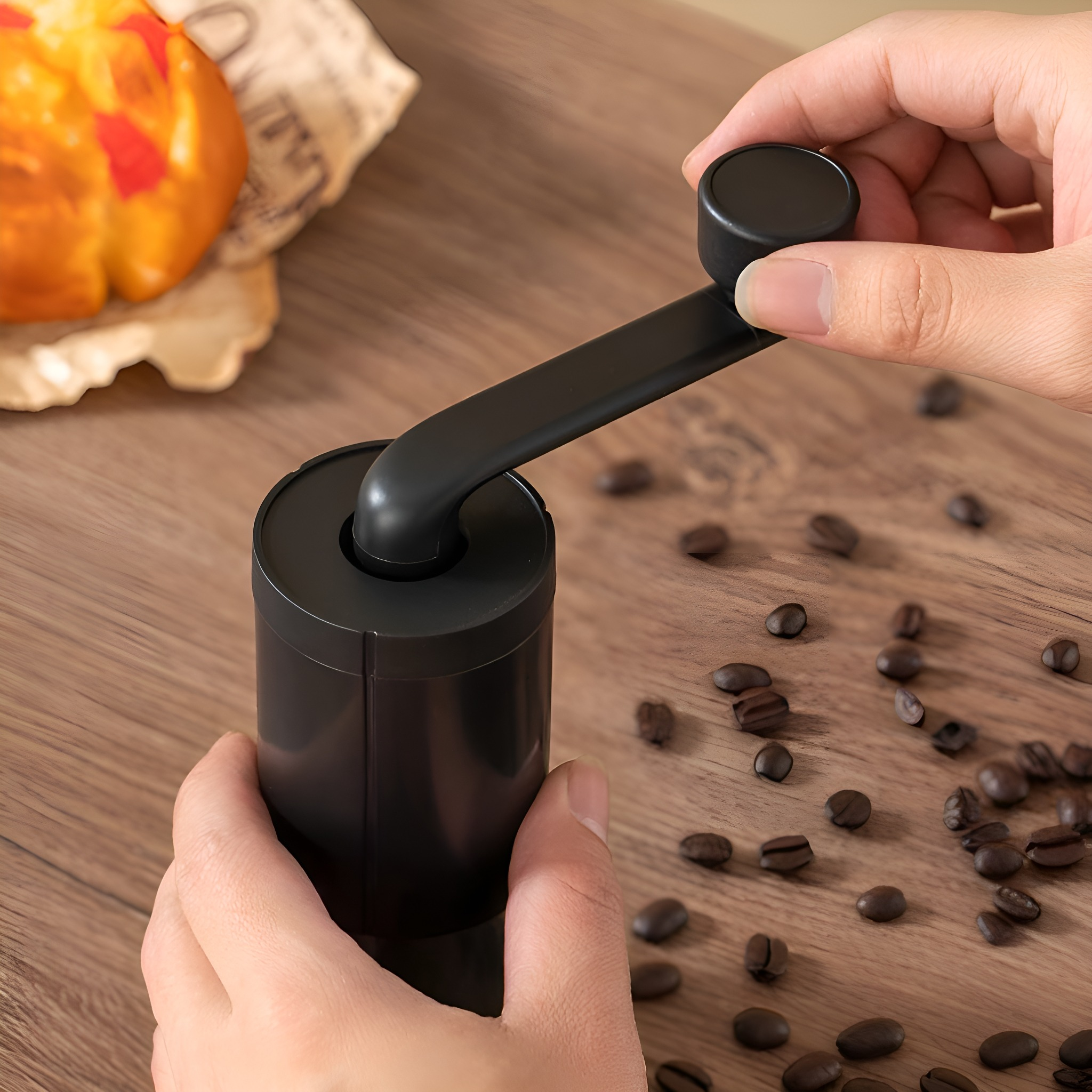 Hände einer Person, die Kaffeebohnen mit einer schwarzen manuellen Mühle mahlen, mit Kaffeebohnen auf Holzoberfläche.