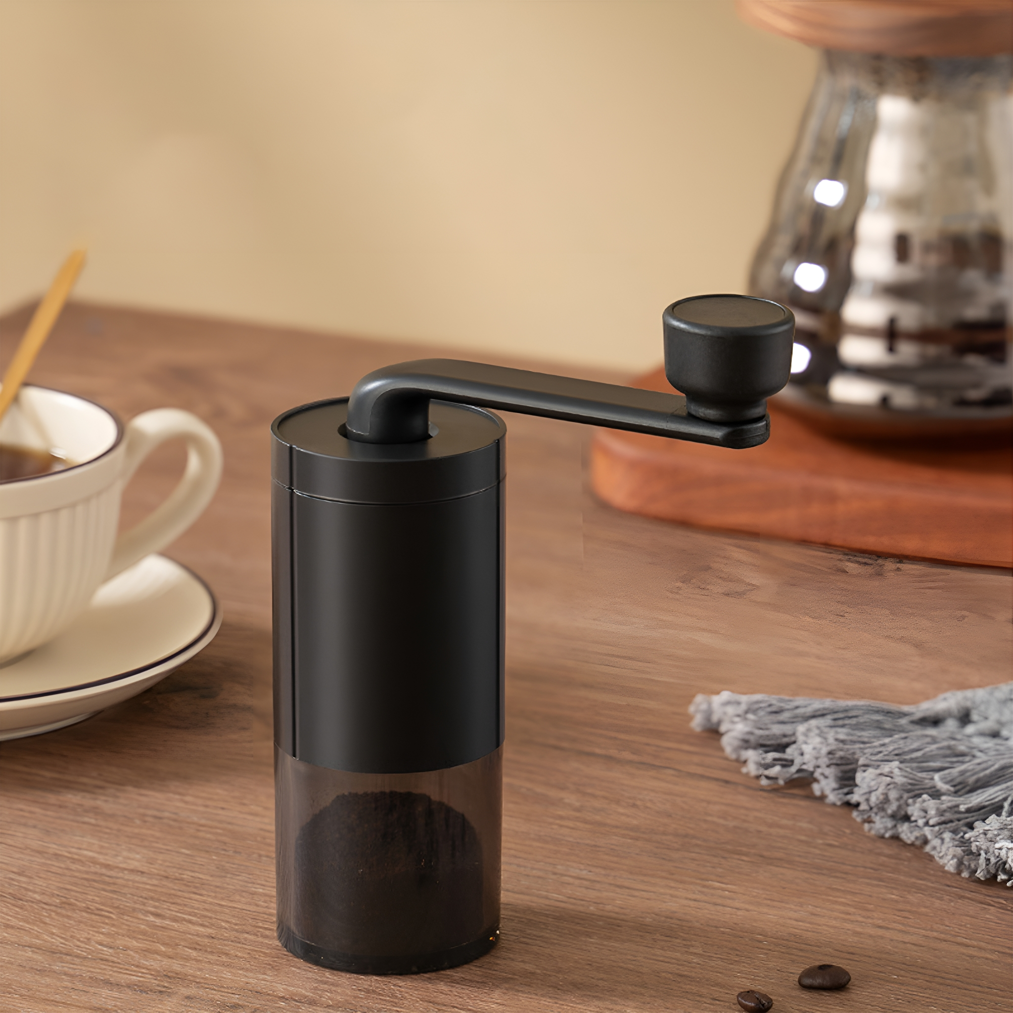 Schwarze manuelle Kaffeemühle mit klarer Basis, auf einem Holztisch.