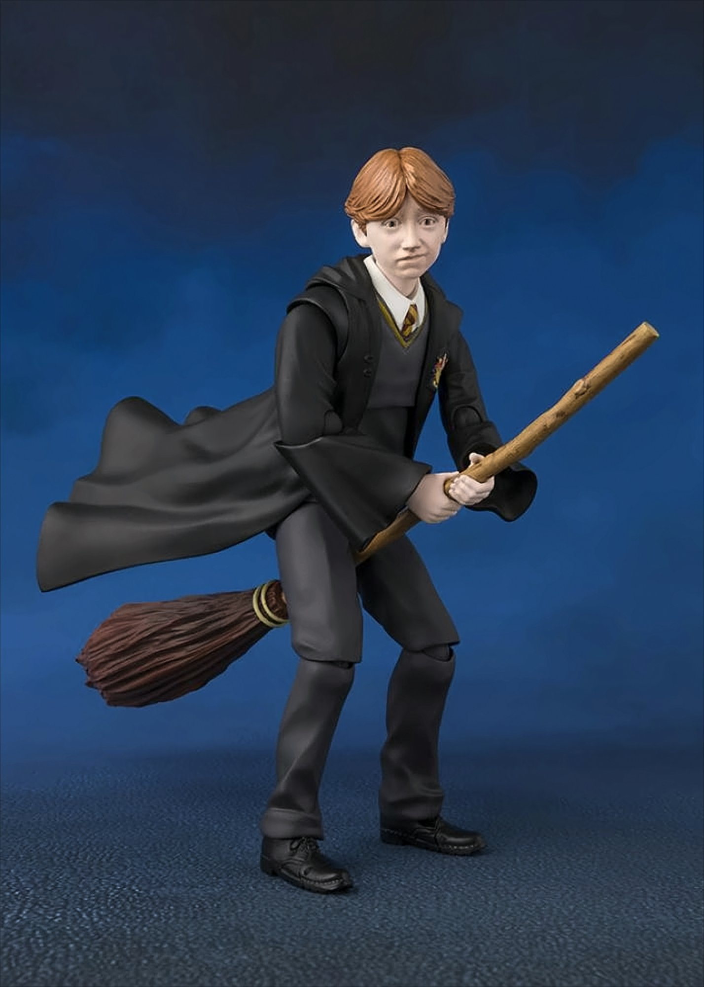 Eine Ron Weasley Figur in schwarzen Roben, einen Besen haltend, mit blauem, bewölktem Hintergrund.