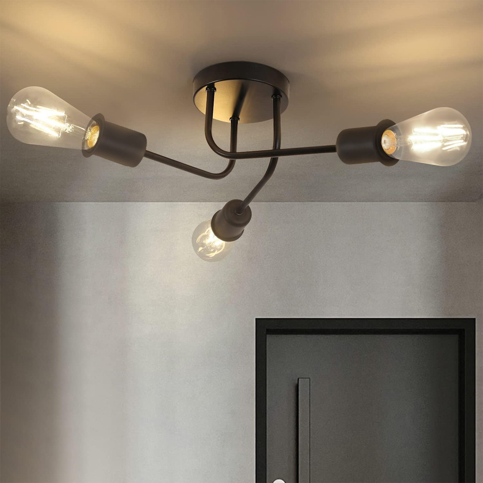 Una lampada da soffitto a tre lampadine con lampadine a vista, contro un muro grigio.