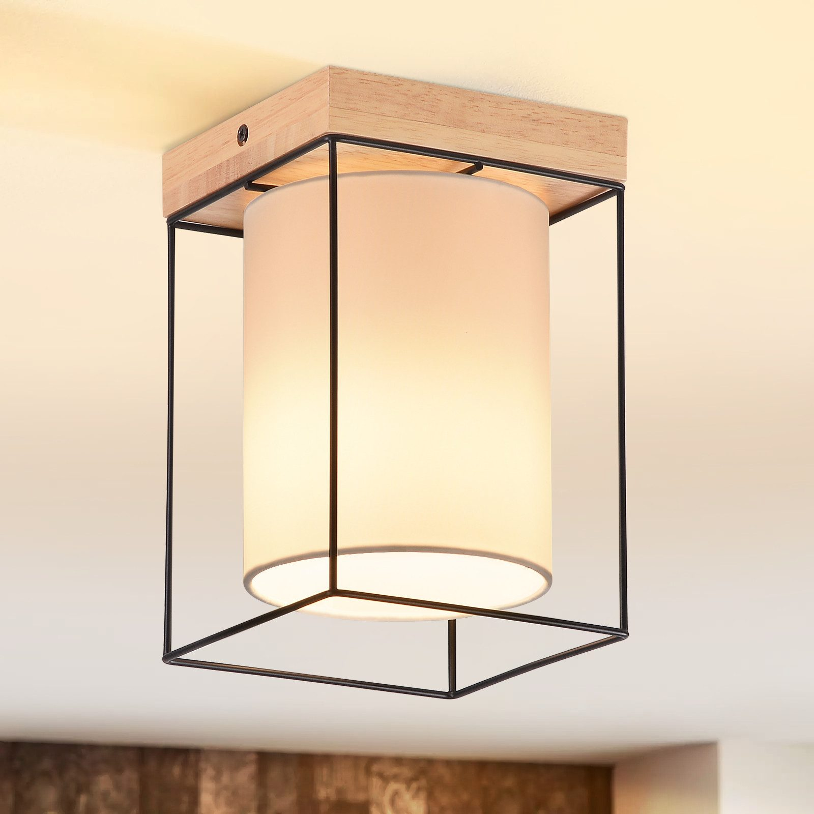 Lampada da soffitto con base in legno, struttura in metallo nero e paralume cilindrico bianco, che illumina una stanza.