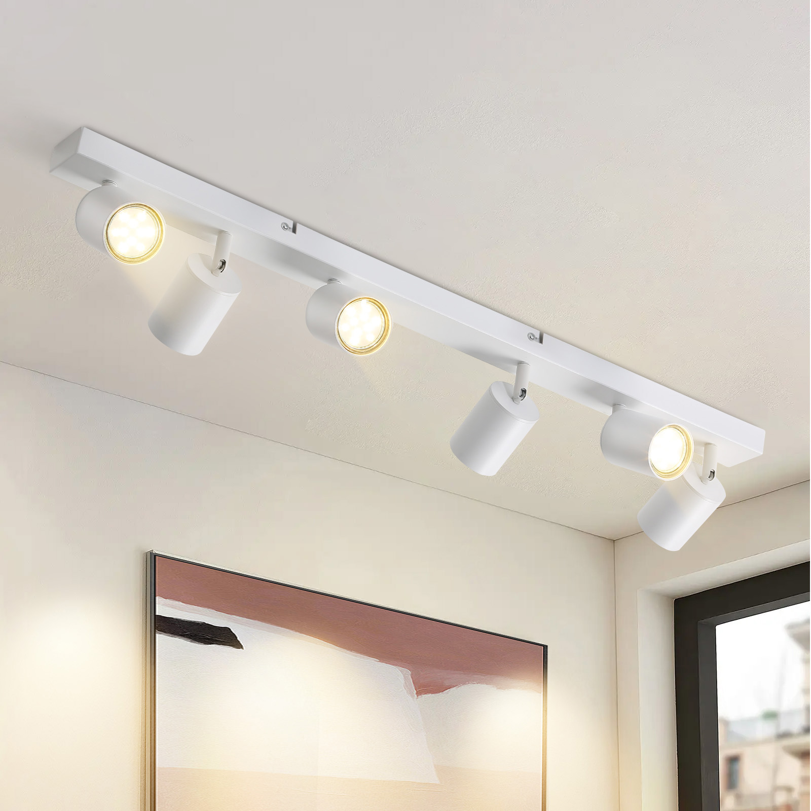 Illuminazione a binario bianca con quattro faretti regolabili su un soffitto bianco. Un quadro appeso al muro.