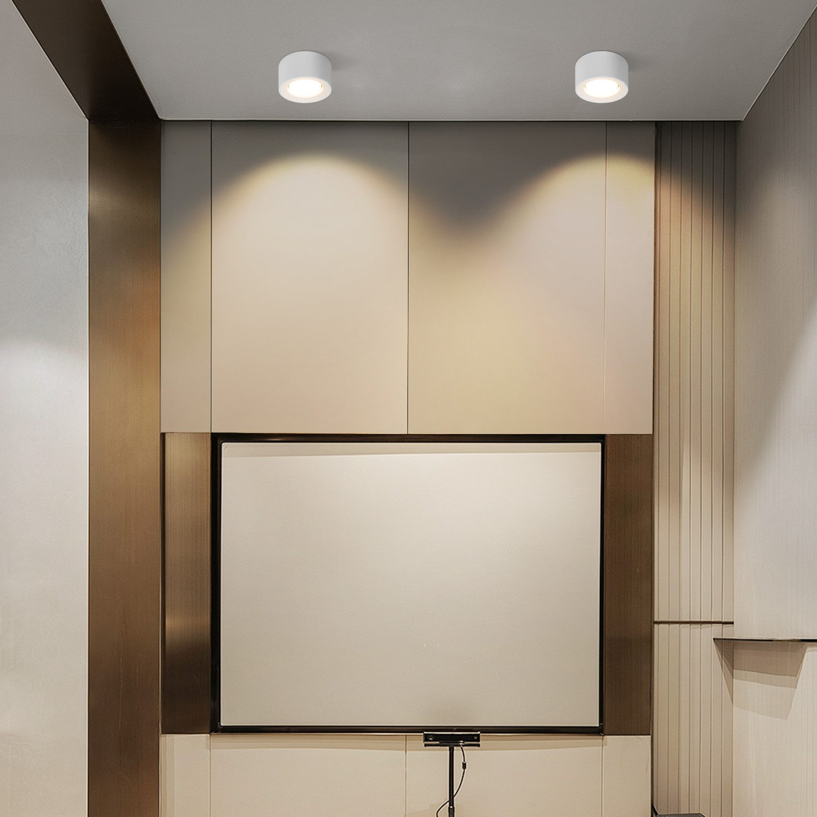 Dwa białe okrągłe światła sufitowe. Światła znajdują się w pokoju z telewizorem i szafkami.