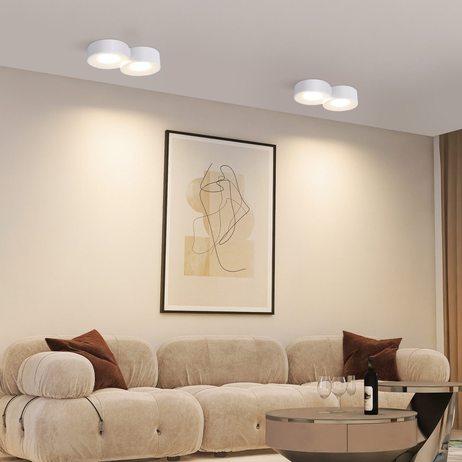 Soggiorno con divano beige, arte murale e due lampade da soffitto bianche.