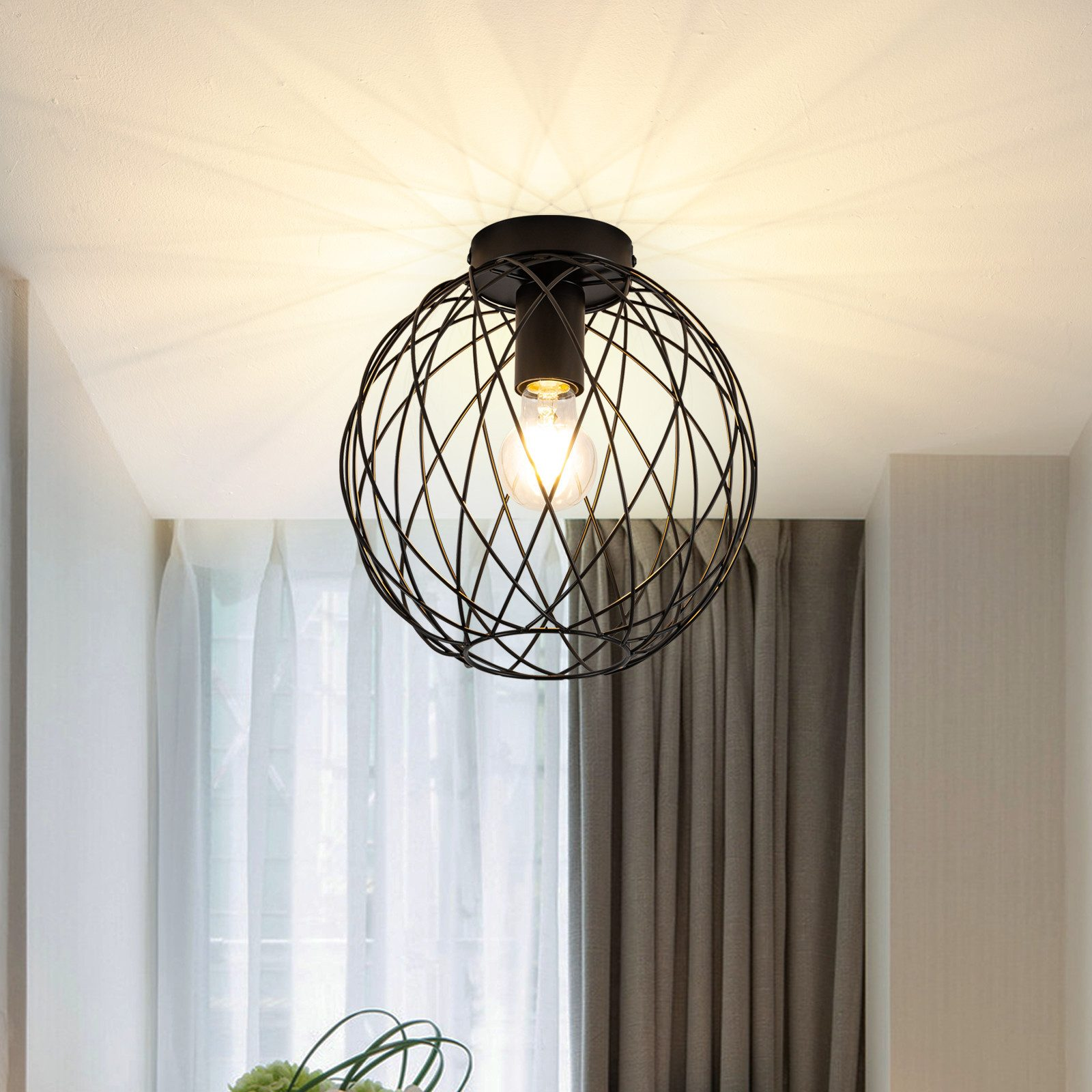 Un apparecchio di illuminazione nero, sferico, a forma di gabbia, pende dal soffitto bianco. È visibile una singola lampadina.