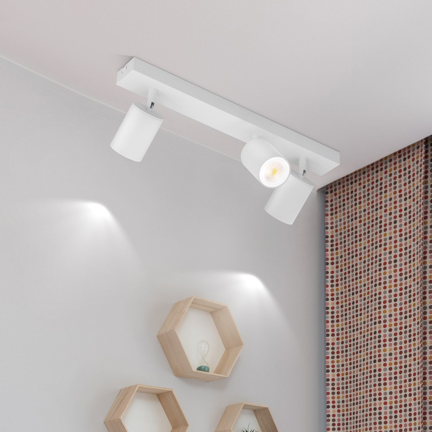 Faretti bianchi a soffitto che illuminano verso il basso. Scaffali esagonali in legno e tenda a fantasia sullo sfondo.