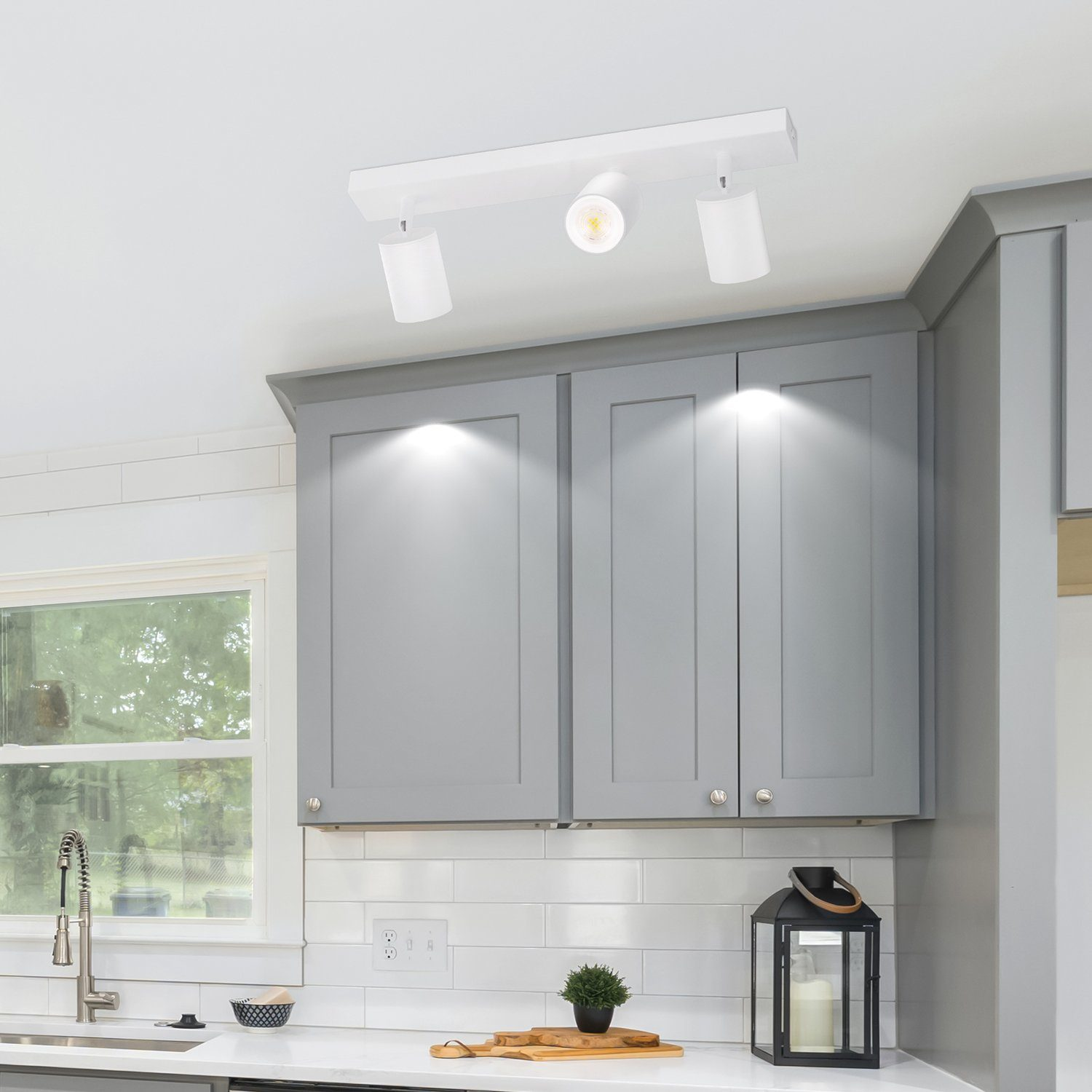 Cucina bianca con mobili grigi e una lampada da soffitto bianca con tre luci.
