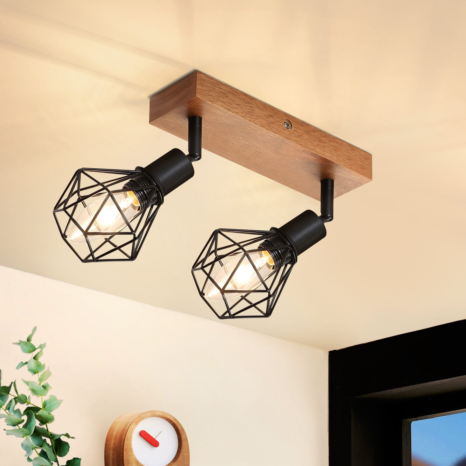 Due faretti neri a gabbia su una trave di legno. Il soffitto è chiaro. Pianta e orologio nell'angolo.