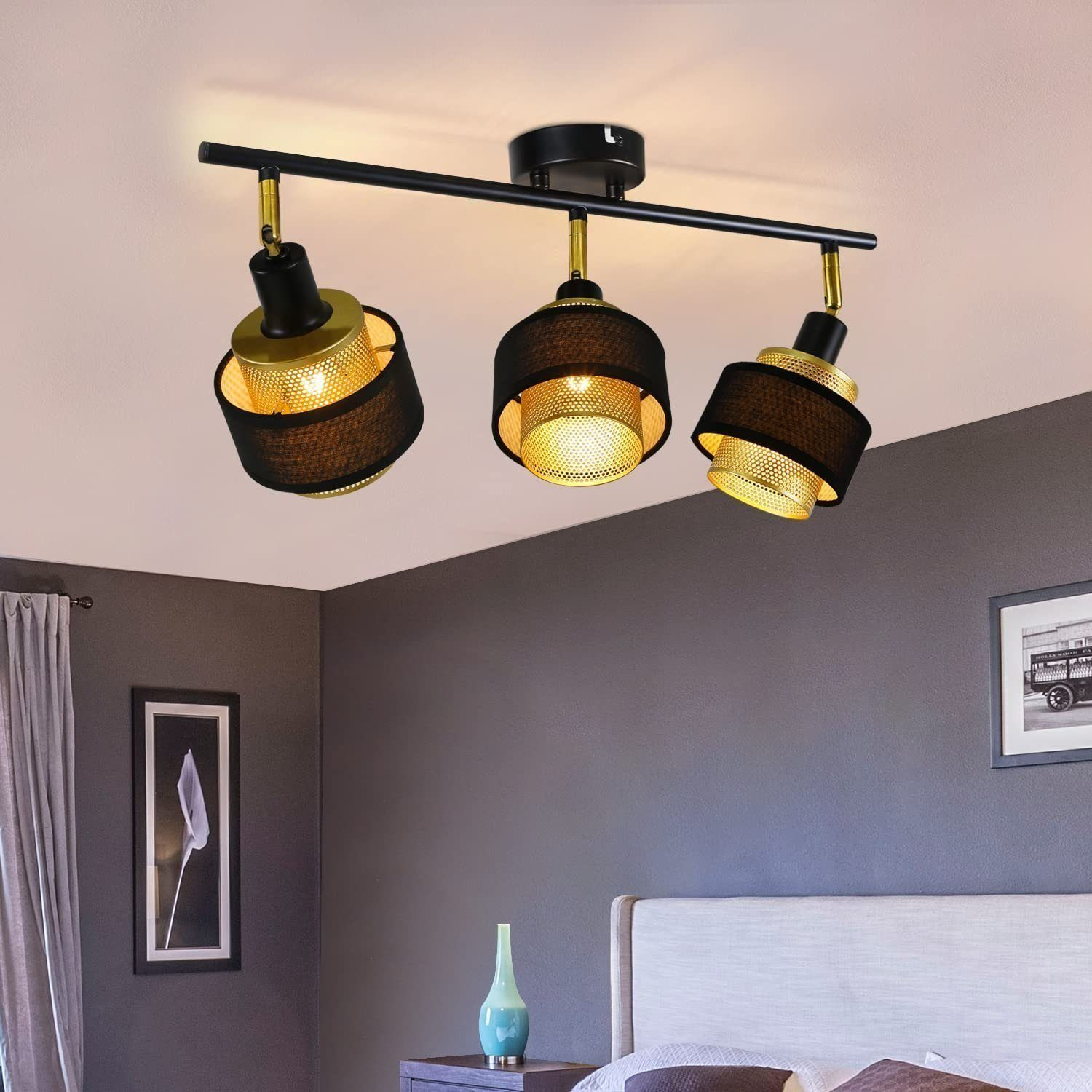 Eine schwarze Deckenleuchte mit drei verstellbaren Strahlern, über einem Bett und Kunstwerk.