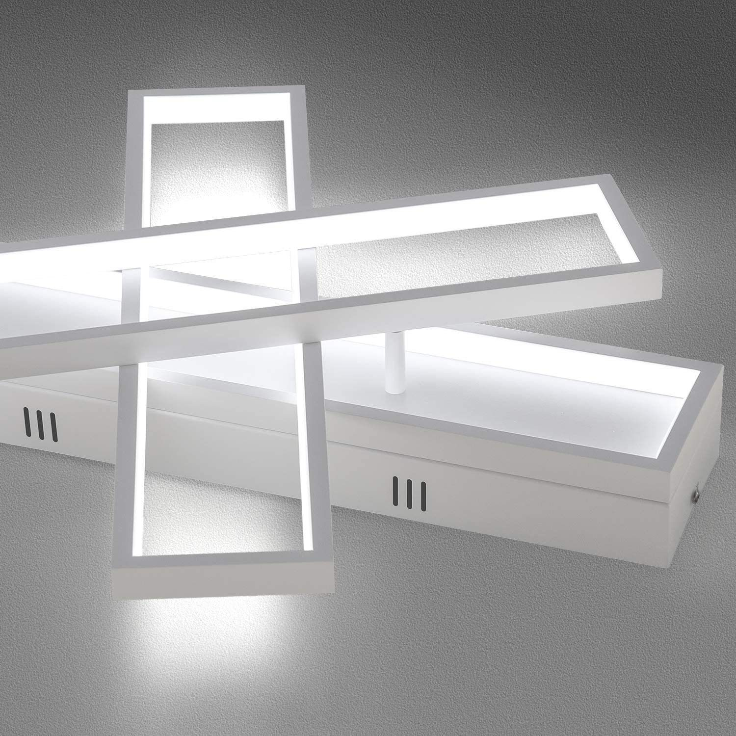 Una plafoniera bianca con un design geometrico. La luce è su un muro grigio.