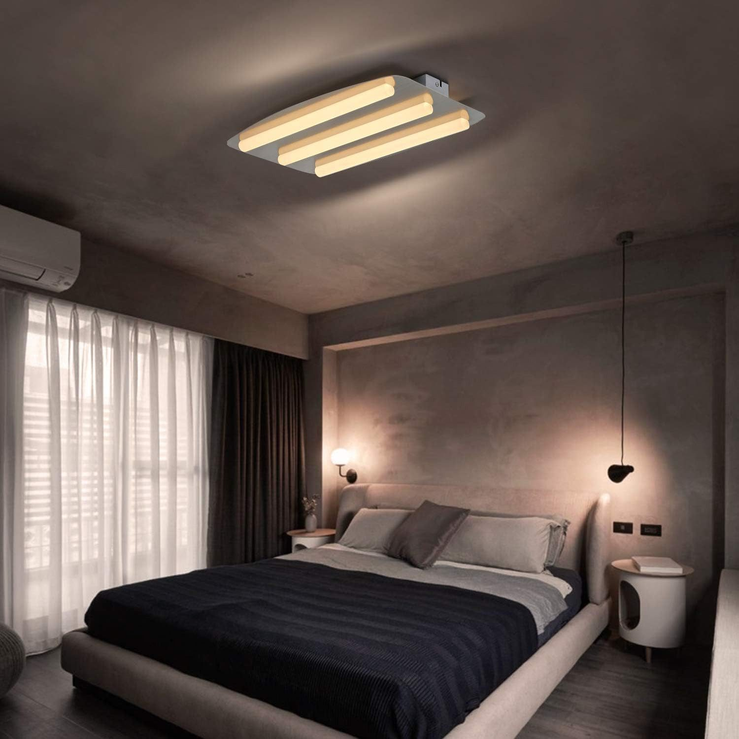Camera da letto con luce a soffitto. Letto con cuscini e coperta, tende e parete bianca.