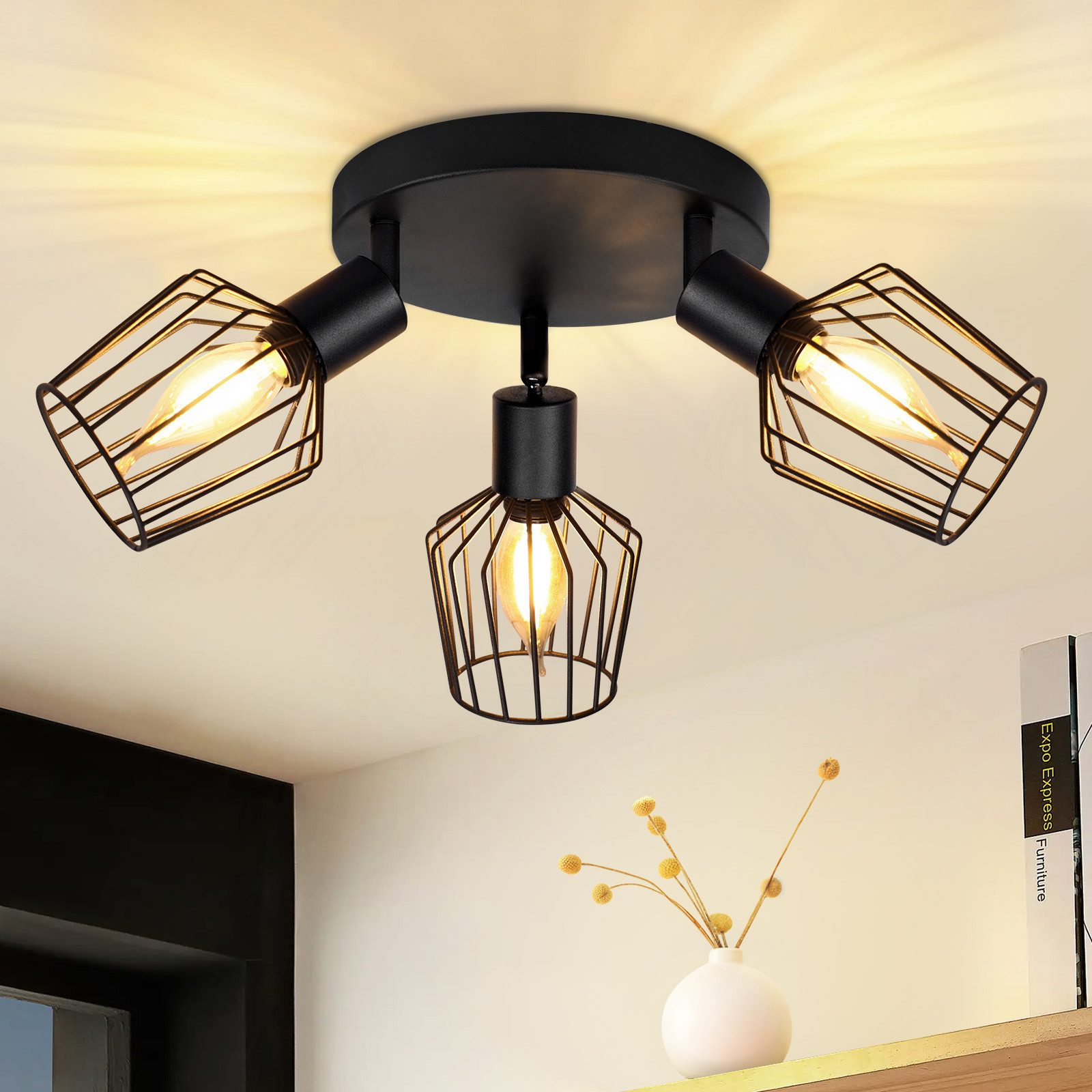 Una plafoniera nera con tre faretti regolabili racchiusi in gabbie metalliche, contro un soffitto bianco.