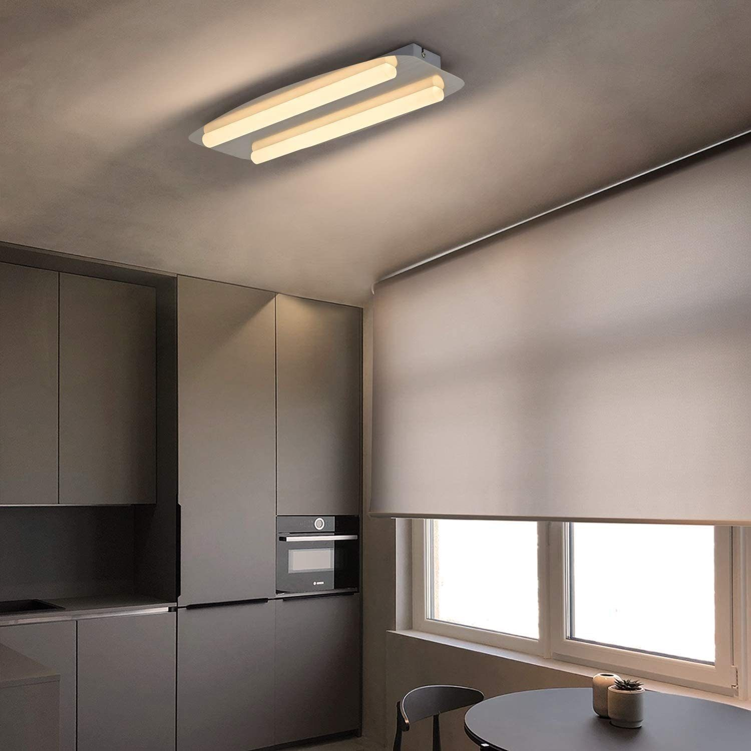 Una cucina con un apparecchio di illuminazione a soffitto bianco, armadi grigi e un tavolo scuro con una sedia.
