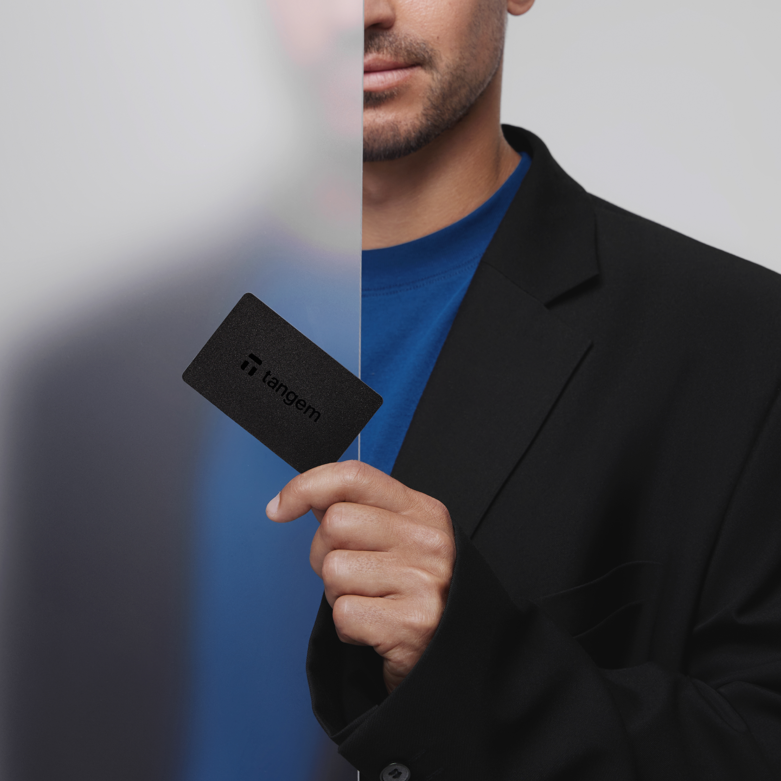 Mężczyzna trzyma czarną kartę z napisem 'tangem'. Karta znajduje się przed matowym szkłem.