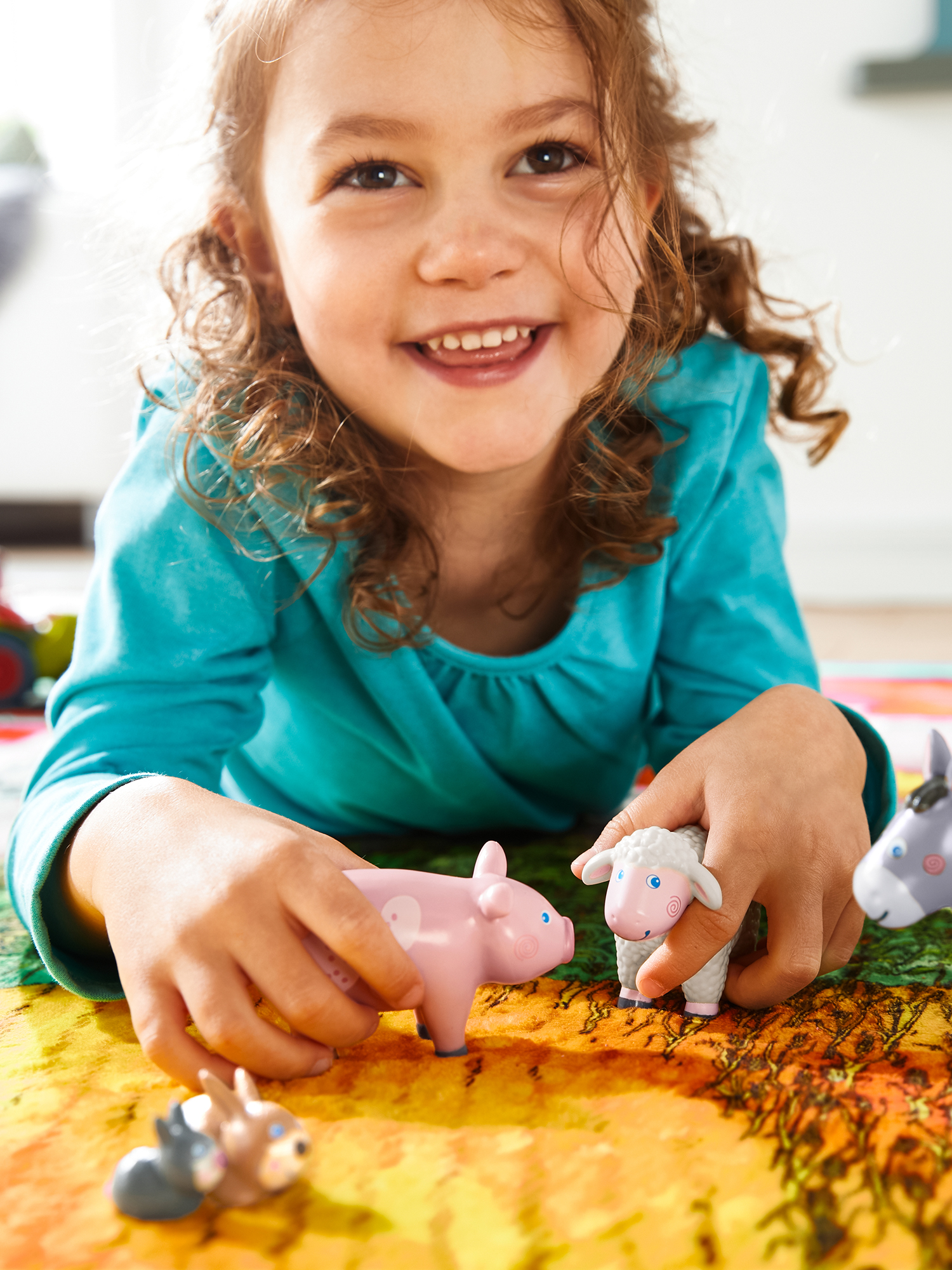 Ein junges Mädchen lächelt, während es mit Spielzeug-Bauernhoftieren spielt. Ein rosa Schwein, ein weißes Schaf und ein grauer Esel.