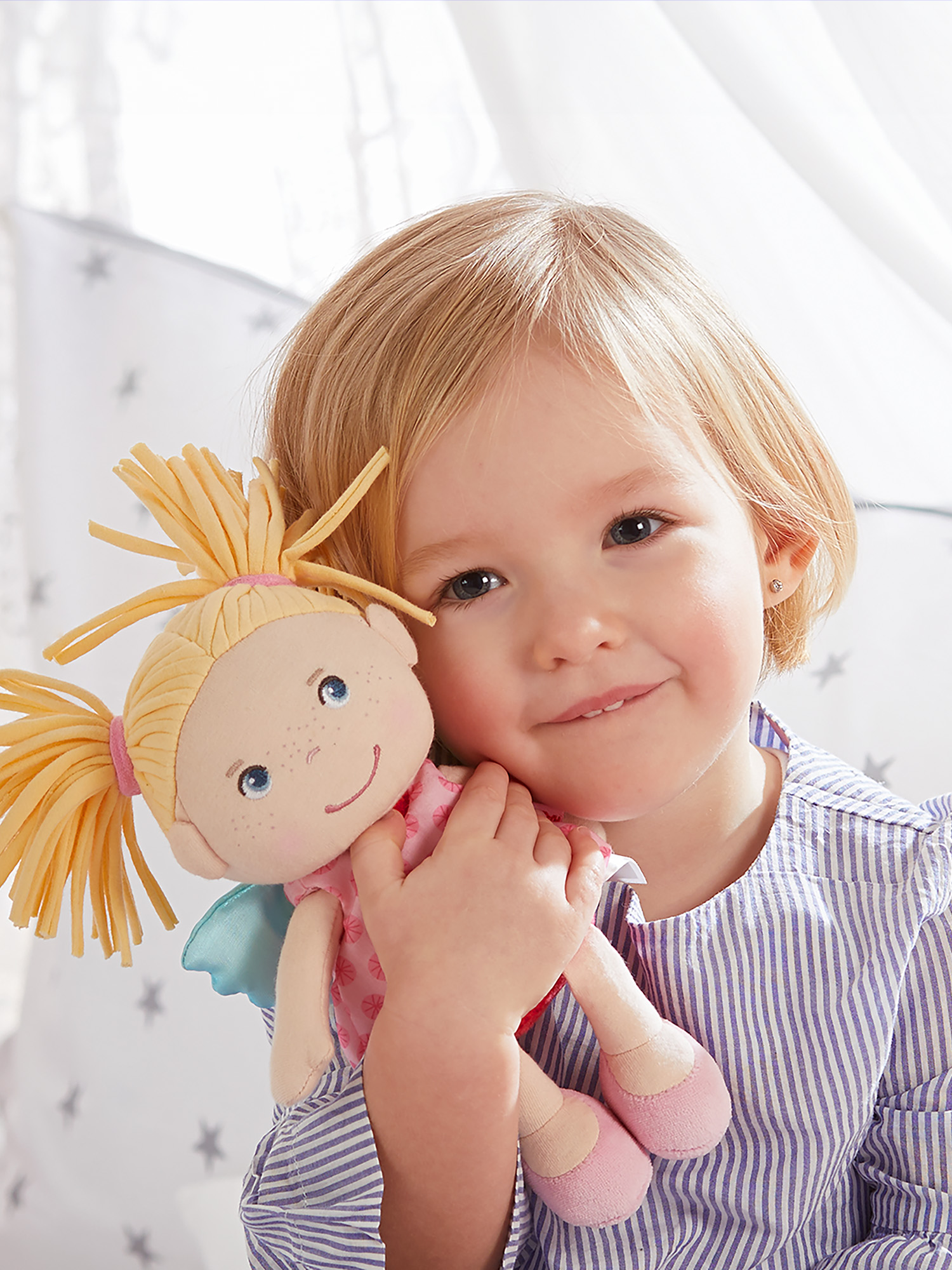 Ein junges Mädchen mit einer Puppe im Arm lächelt in die Kamera.