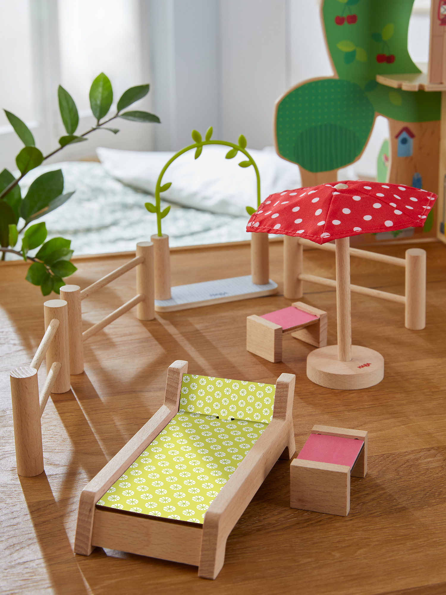 Hölzerne Spielzeugszene: Bett, Regenschirm, Zaun und Bogen. Ein Holzbett mit grün gemusterter Bettwäsche.