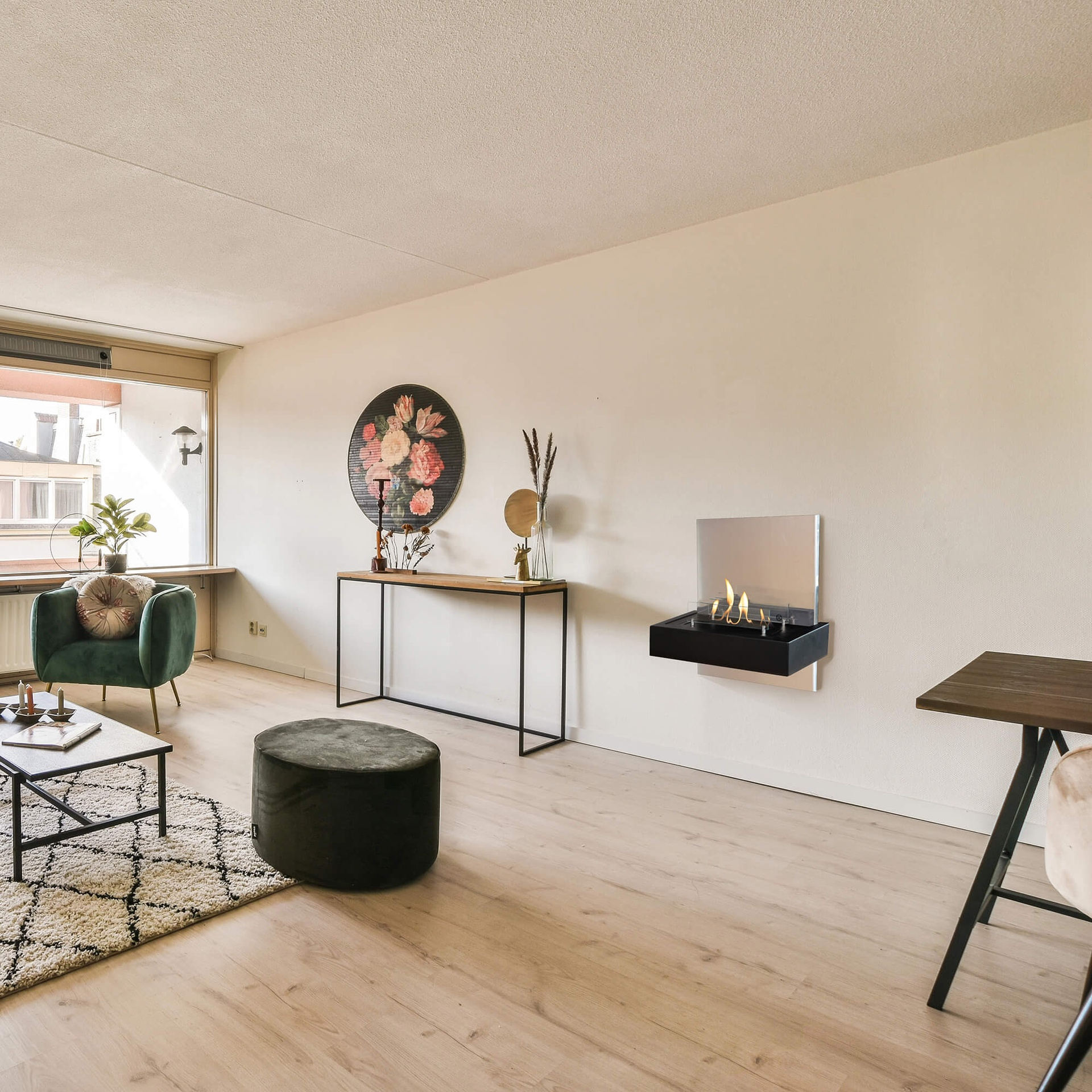 Een woonkamer met een groene fauteuil, een kleed, een salontafel, een bloemenschilderij en een wandhaard.