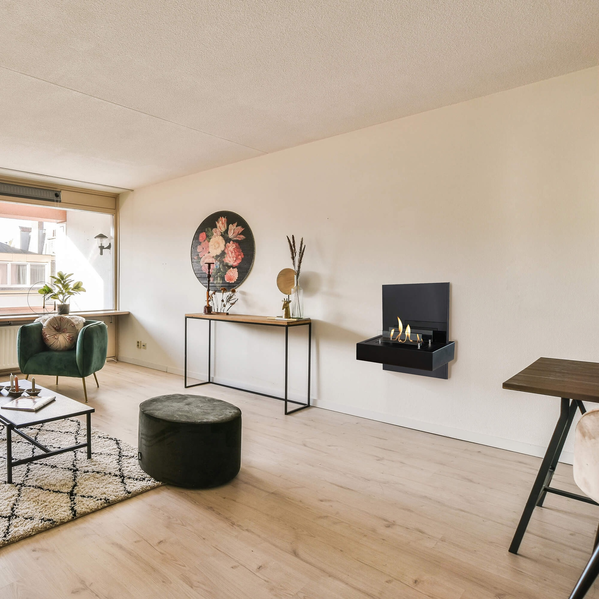 Een woonkamer met een groene fauteuil, een salontafel en een decoratieve open haard aan de muur. Houten vloer en neutrale muur.