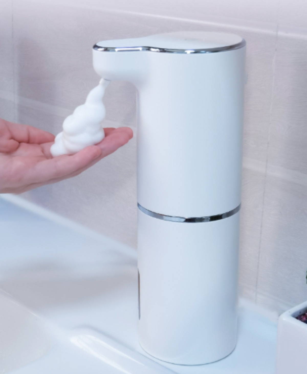 Weißer automatischer Seifenspender gibt Schaum auf eine Hand ab, Badezimmer.