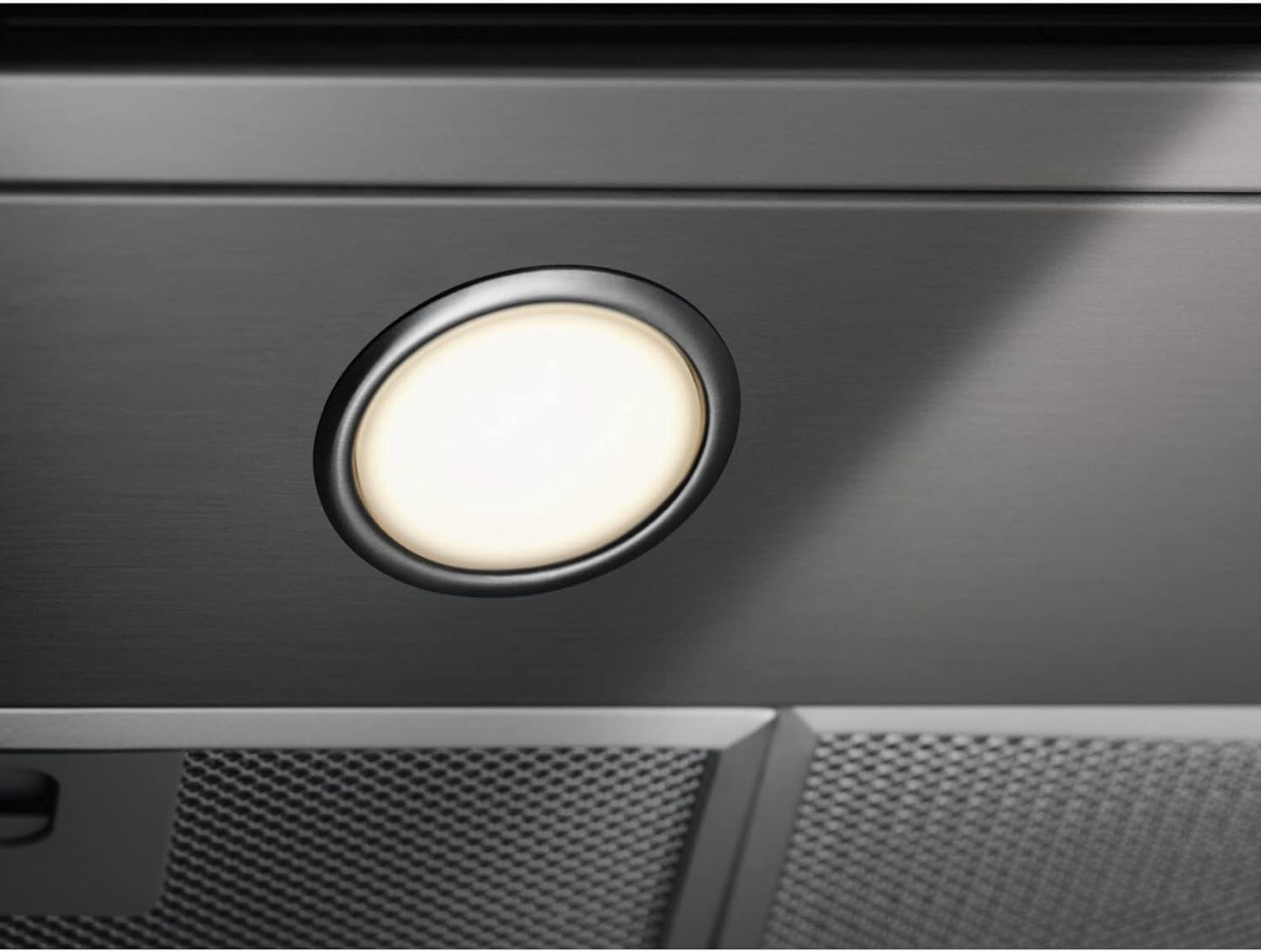 Primer plano de una campana extractora con una luz ovalada. La luz está encendida y rodeada por un marco y panel de metal oscuro.