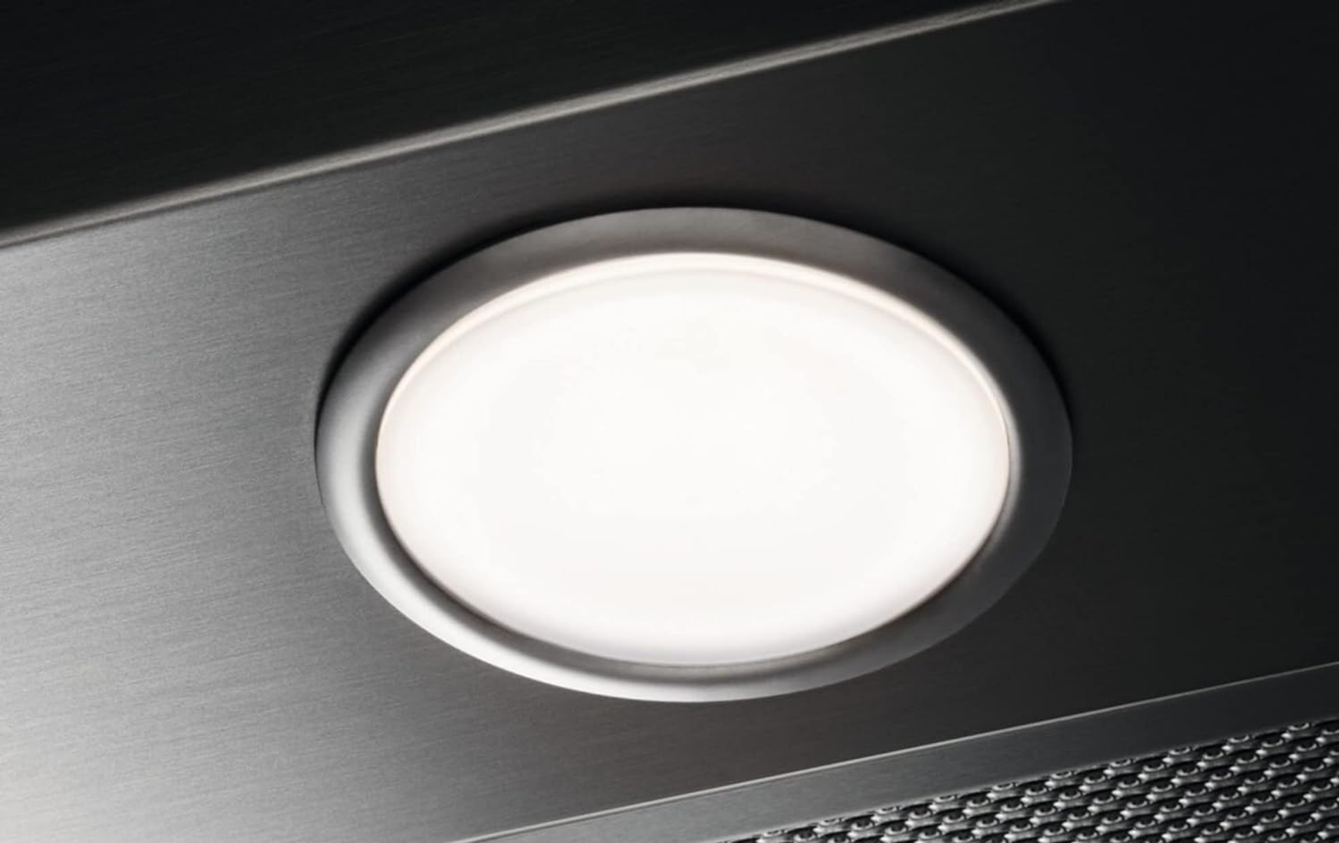 Primer plano de una luminaria circular brillante incrustada en una superficie de metal cepillado. La luz es blanca, rodeada por un anillo metálico.
