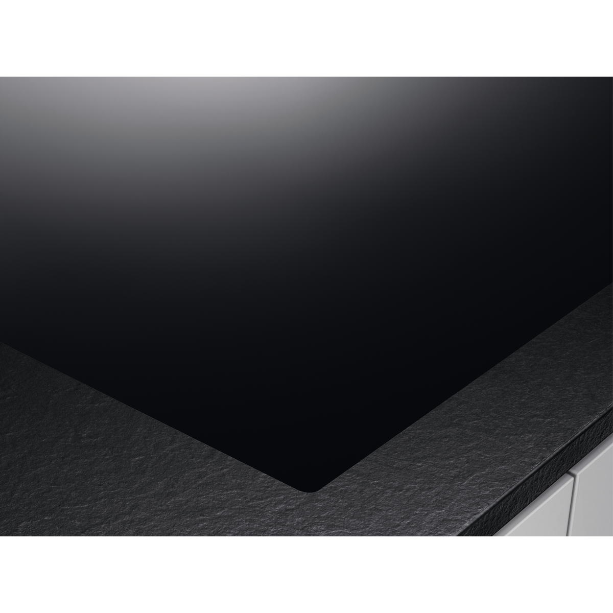 Un primo piano di un piano cottura in ceramica nero. Ha una superficie liscia e un bordo grigio scuro.