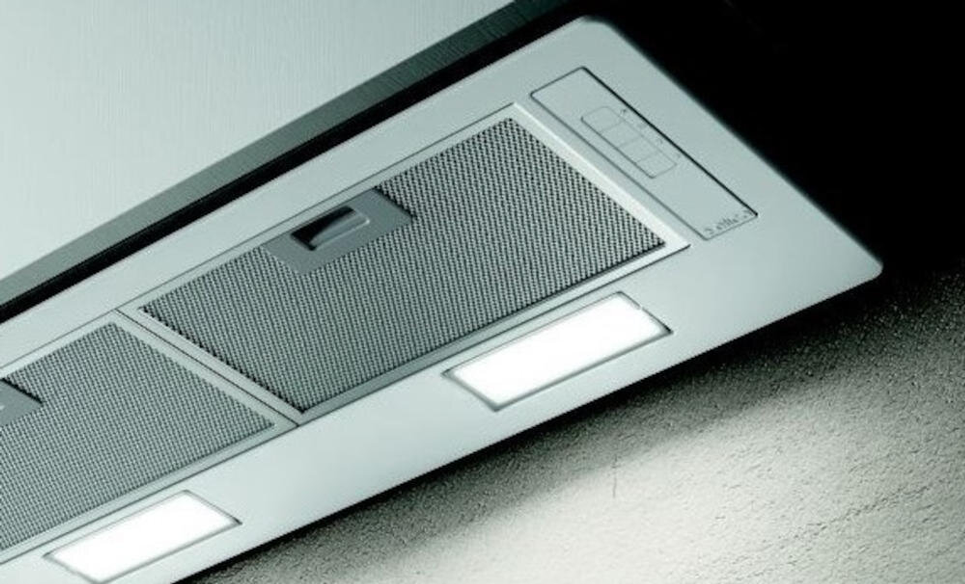 Un primo piano di una cappa da cucina con luci e un filtro a rete. La cappa è argento e bianca.