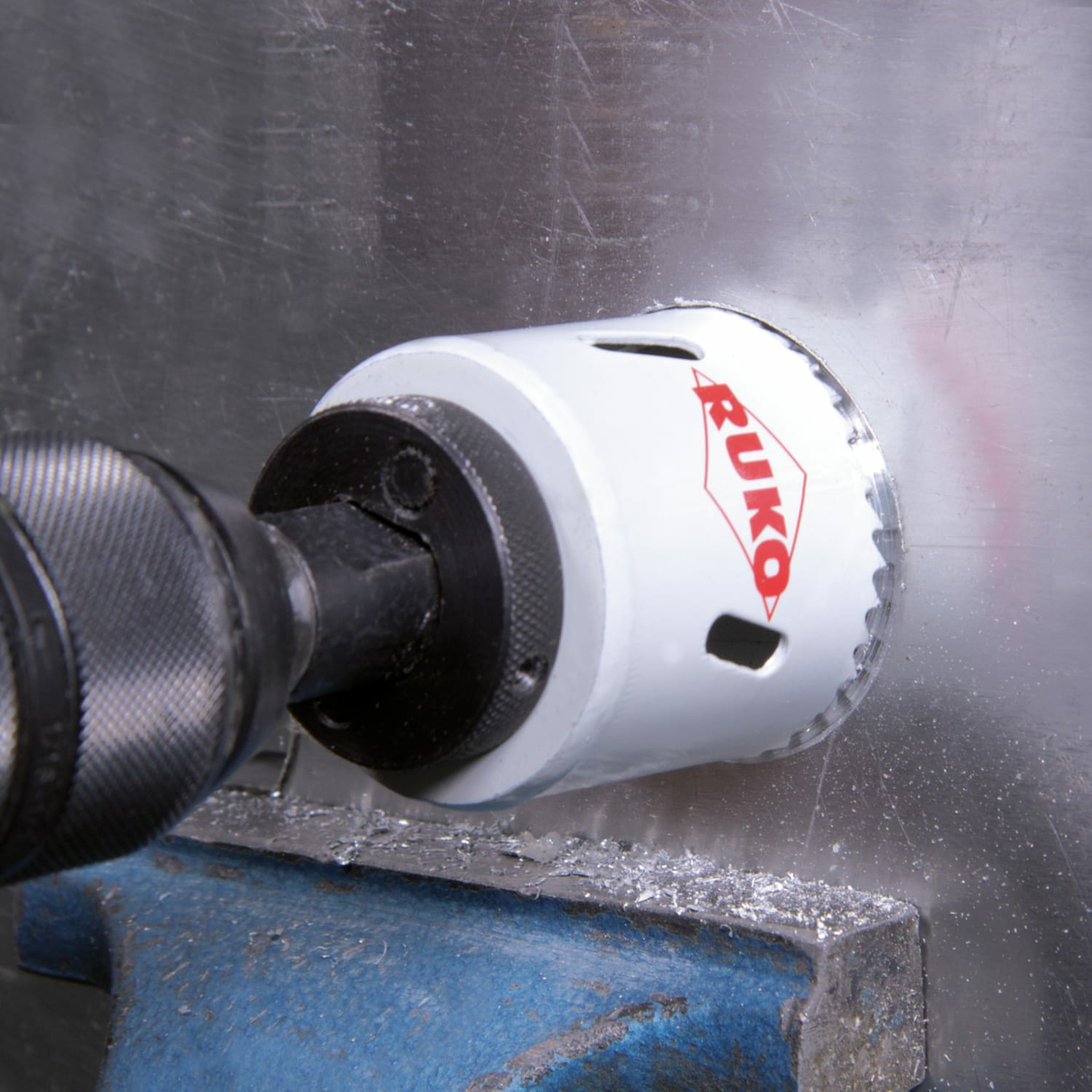 Wiertło wierci otwór w srebrnej blasze za pomocą piły otwornicy RUKO.