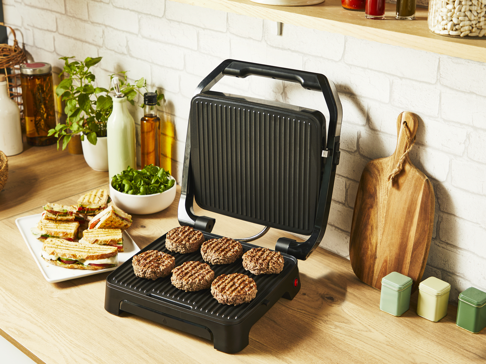 Ein offener schwarzer Grill mit Burgern und Zutaten auf einer Holz-Arbeitsplatte.