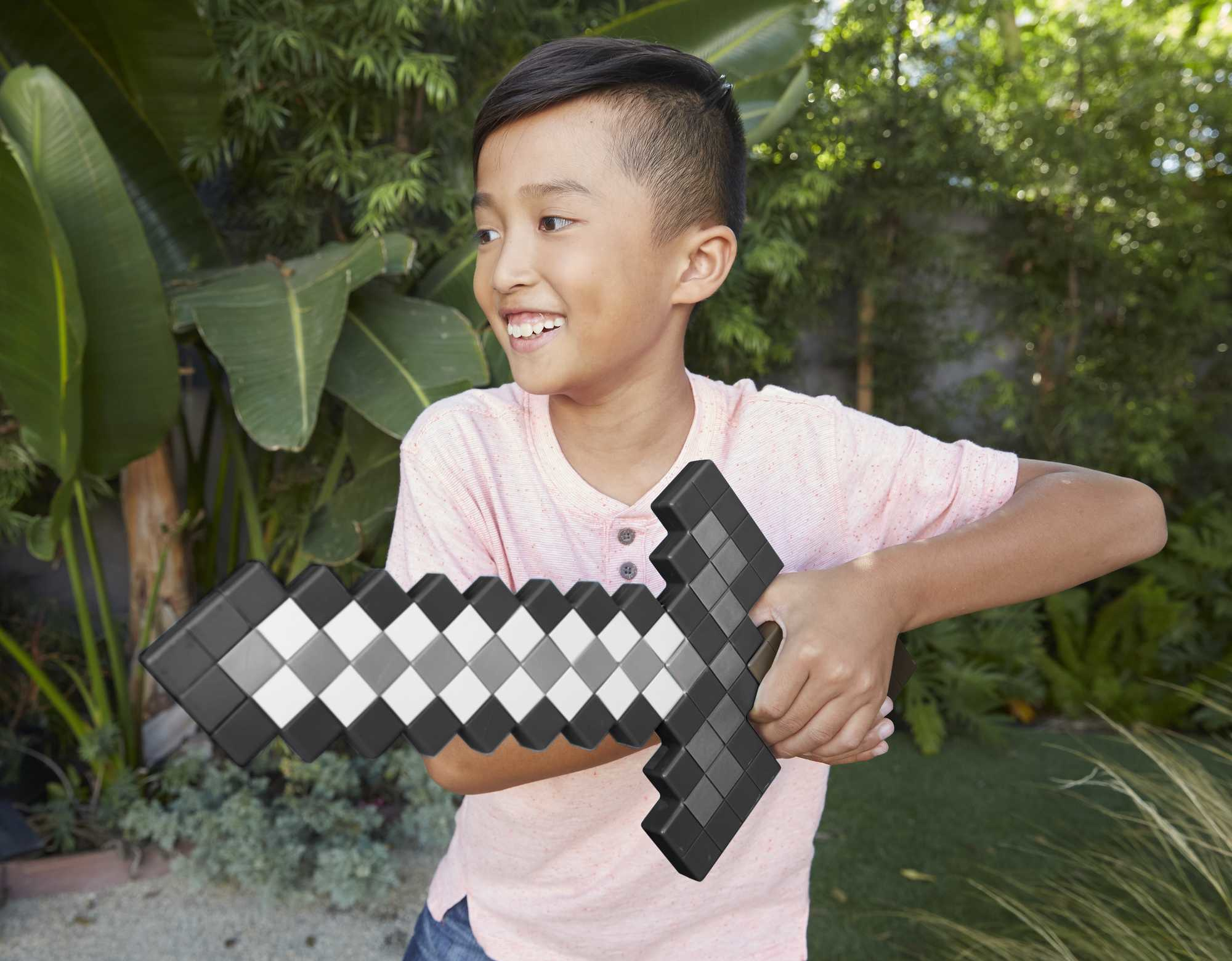 Junge hält ein pixeliges Minecraft-Schwert, lächelt, vor grünem Hintergrund.