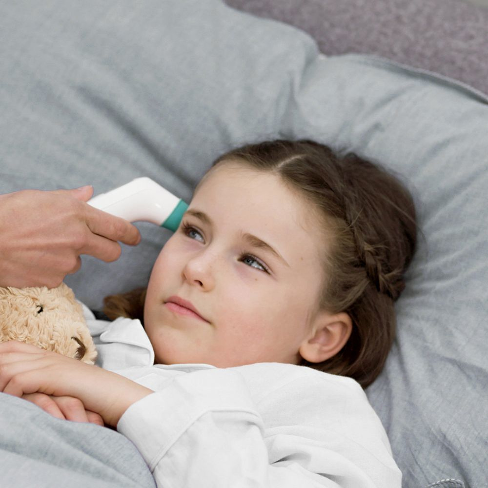 Dziecko leży w łóżku, a ręka trzyma termometr na jej czole. Dziecko patrzy w górę.