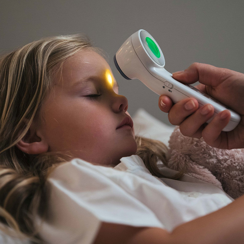 Czoło dziecka skanowane białym termometrem, z zielonym światłem.