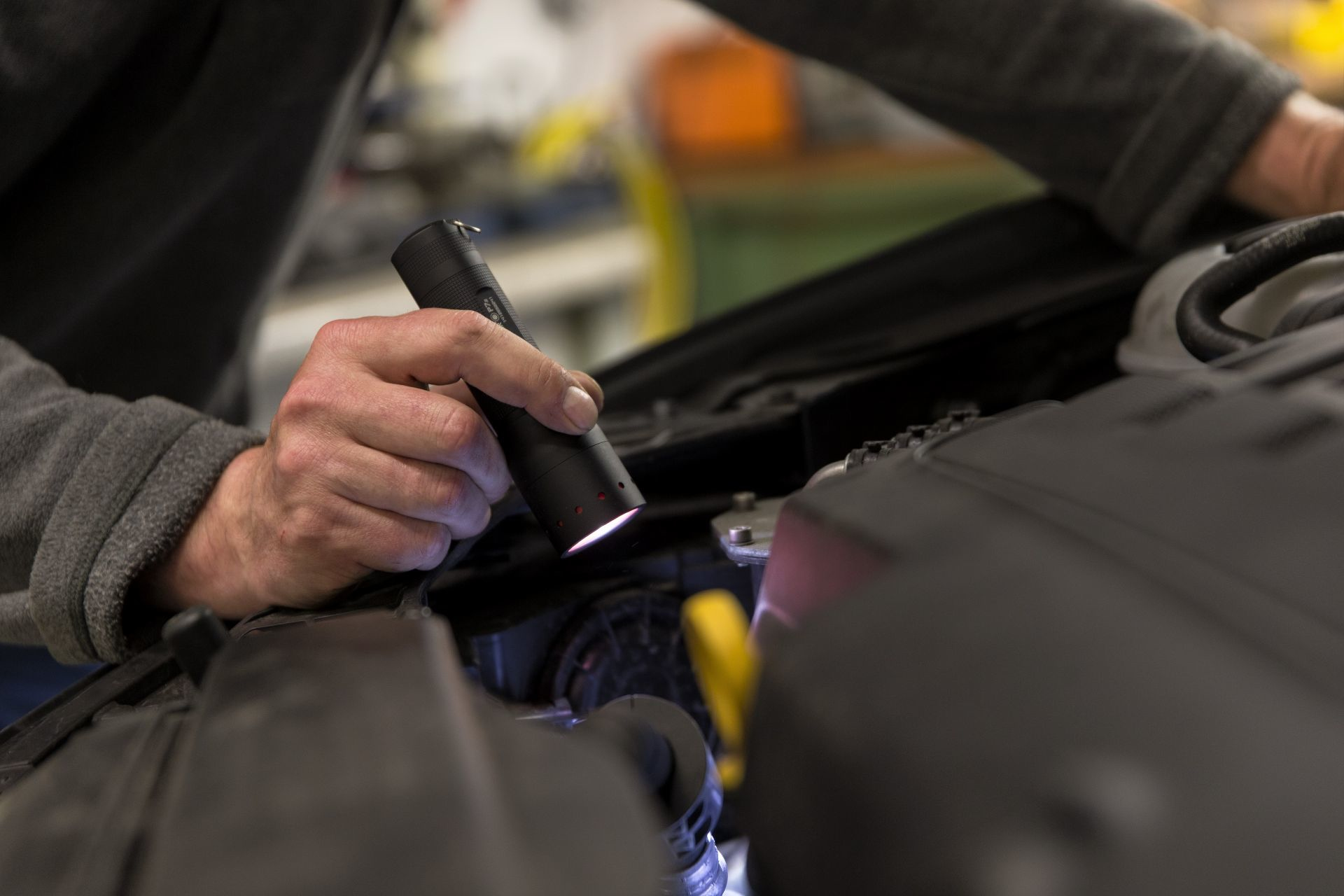 Osoba trzymająca latarkę, sprawdzająca silnik samochodu w garażu.