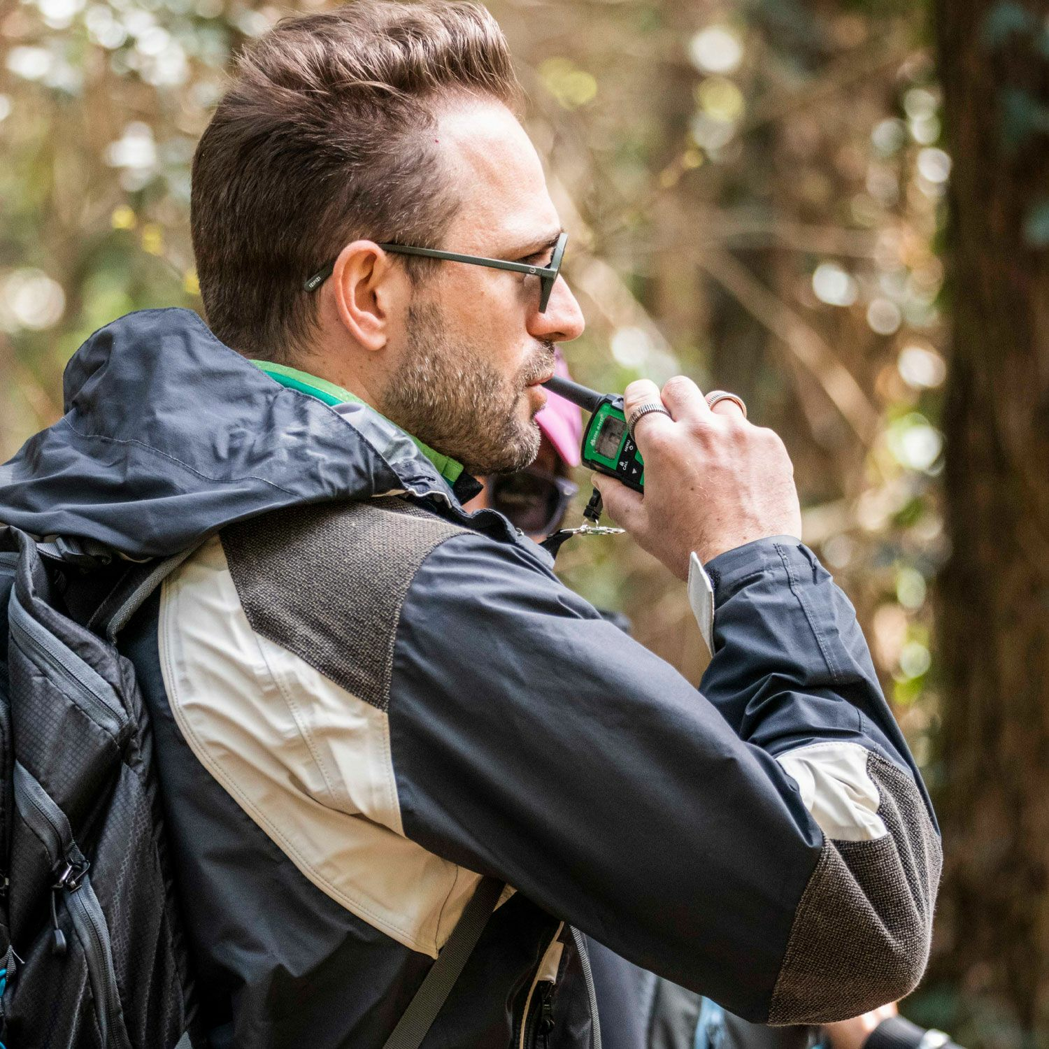 Mężczyzna w okularach przeciwsłonecznych i kurtce na zewnątrz, trzymający w ustach e-papierosa.