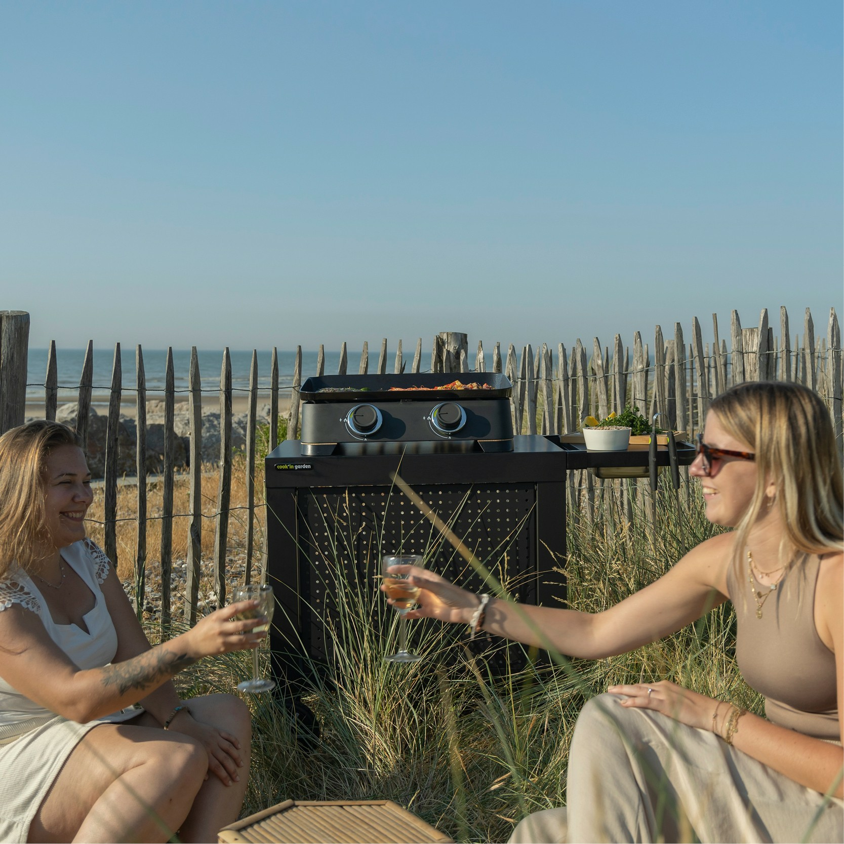 Dwie kobiety wznoszą toast kieliszkami wina przed grillem na plaży.
