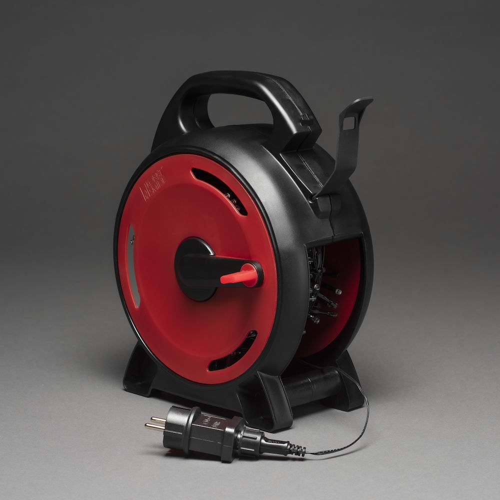 Schwarz-rote Kabeltrommel. Griff und Stecker sichtbar. Grauer Hintergrund, Seitenansicht.