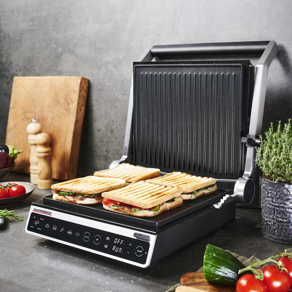 Une presse à panini avec des sandwichs, des légumes et des planches en bois sur une table.