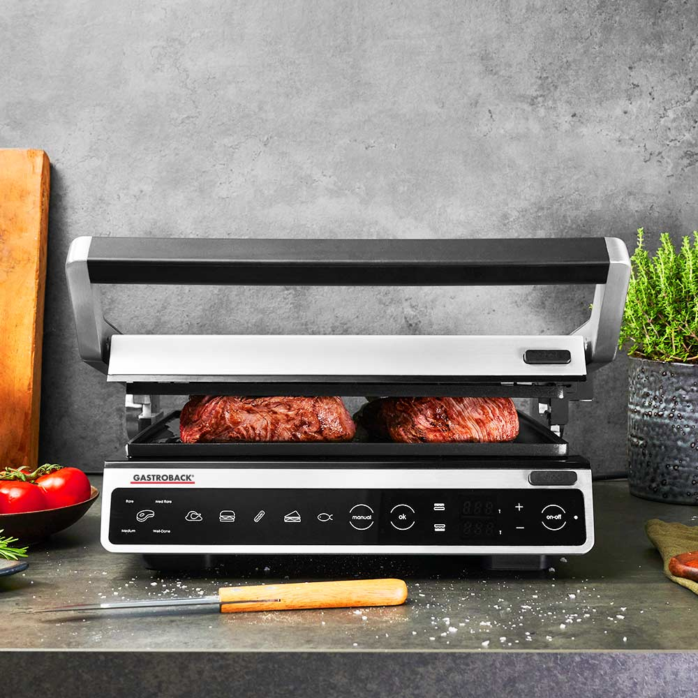Gril d'intérieur avec des steaks en cuisson. Le gril est fermé, et les commandes sont visibles.