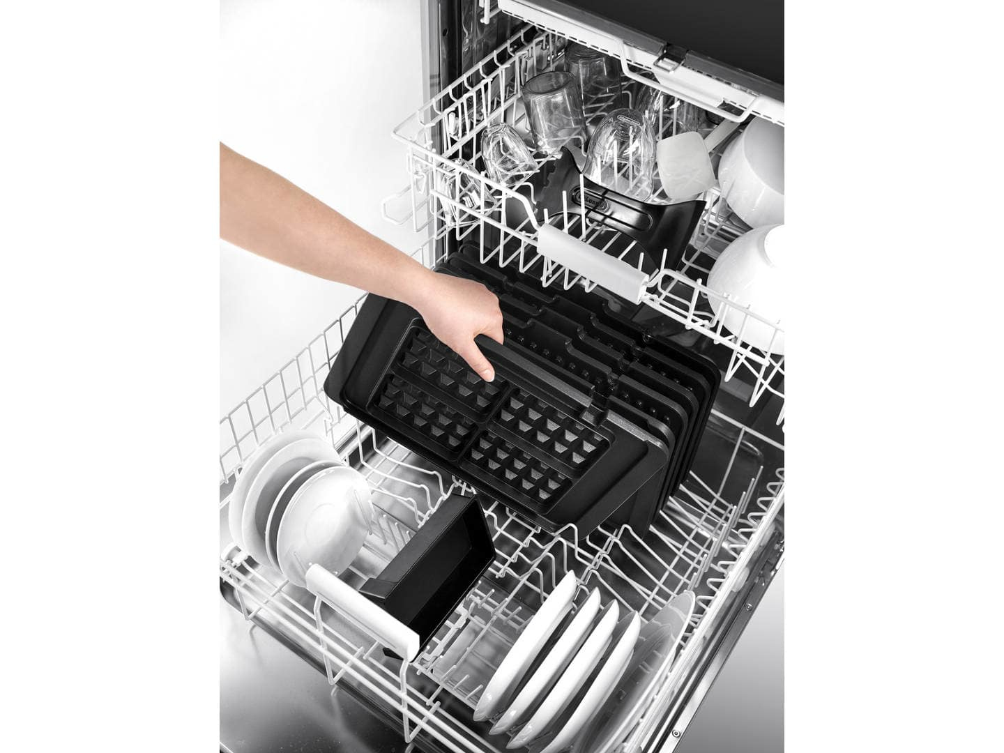 Die Hand einer Person, die einen schwarzen Waffeleisen in eine Spülmaschine mit Geschirr legt.