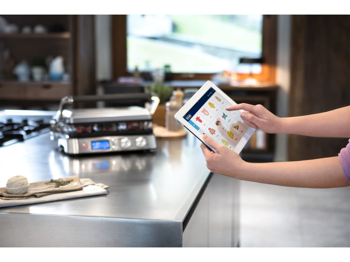 Hände, die ein Tablet benutzen, um einen Grill in der Küche zu steuern.