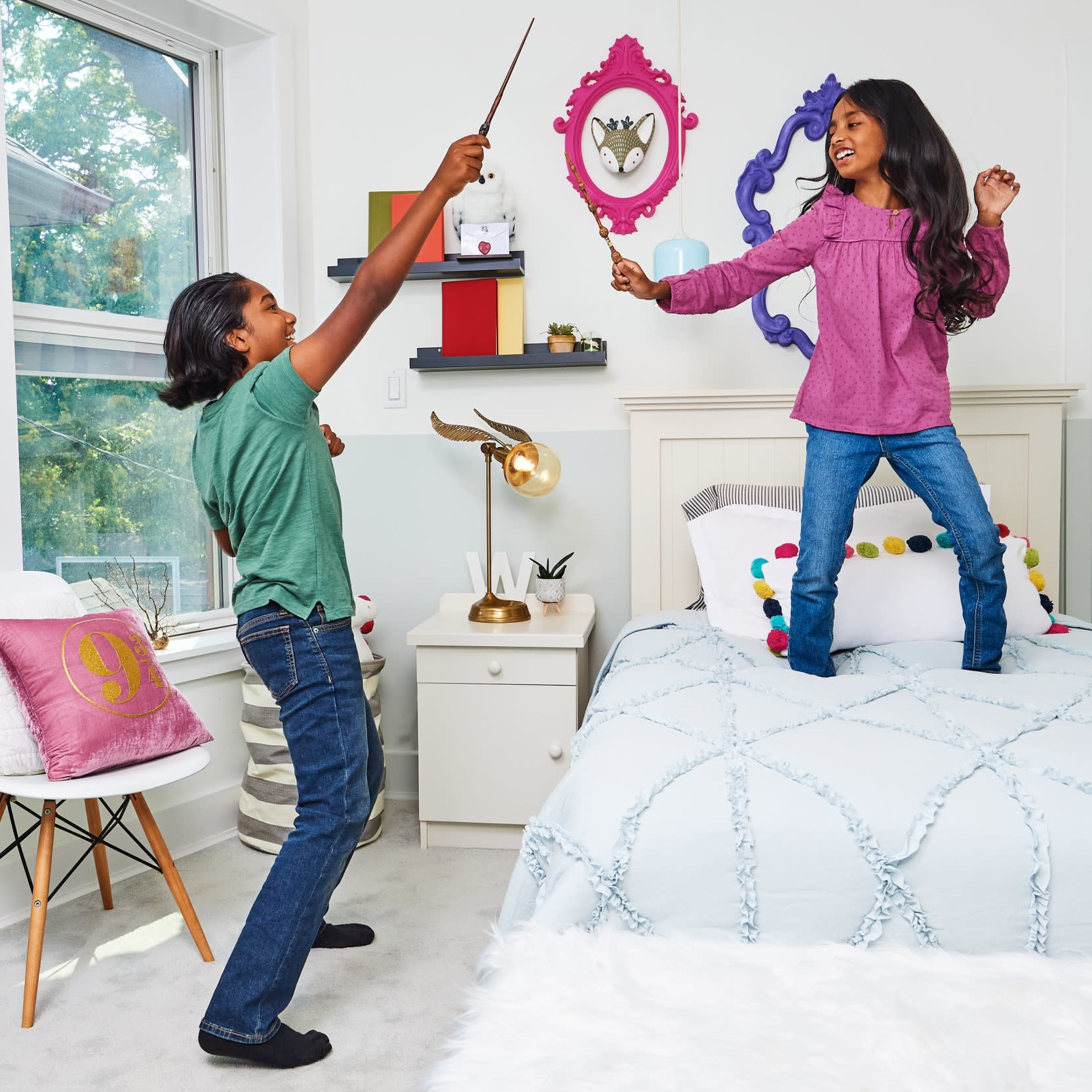 Dwoje dzieci w sypialni bawiących się różdżkami, jedno na łóżku, drugie stojące na podłodze.